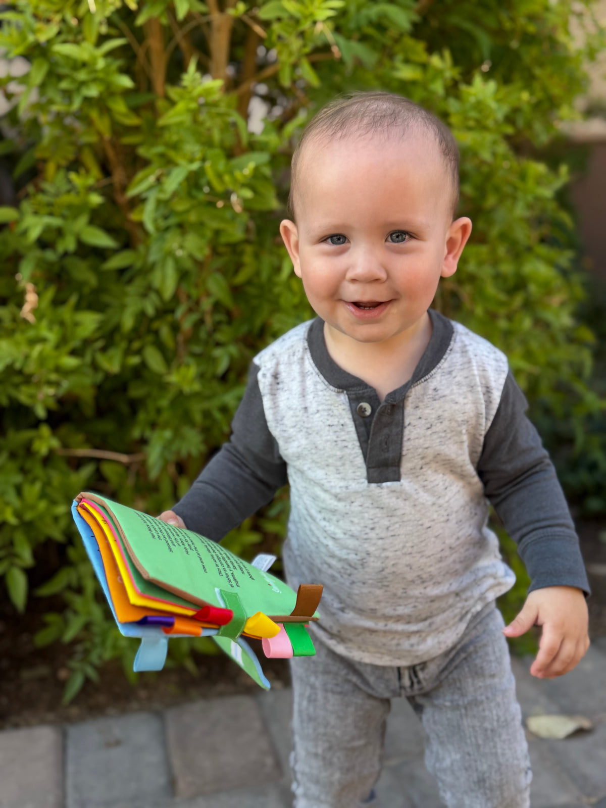 Baby holding an illustrated fabric Mary colors book with multicolor page edges.