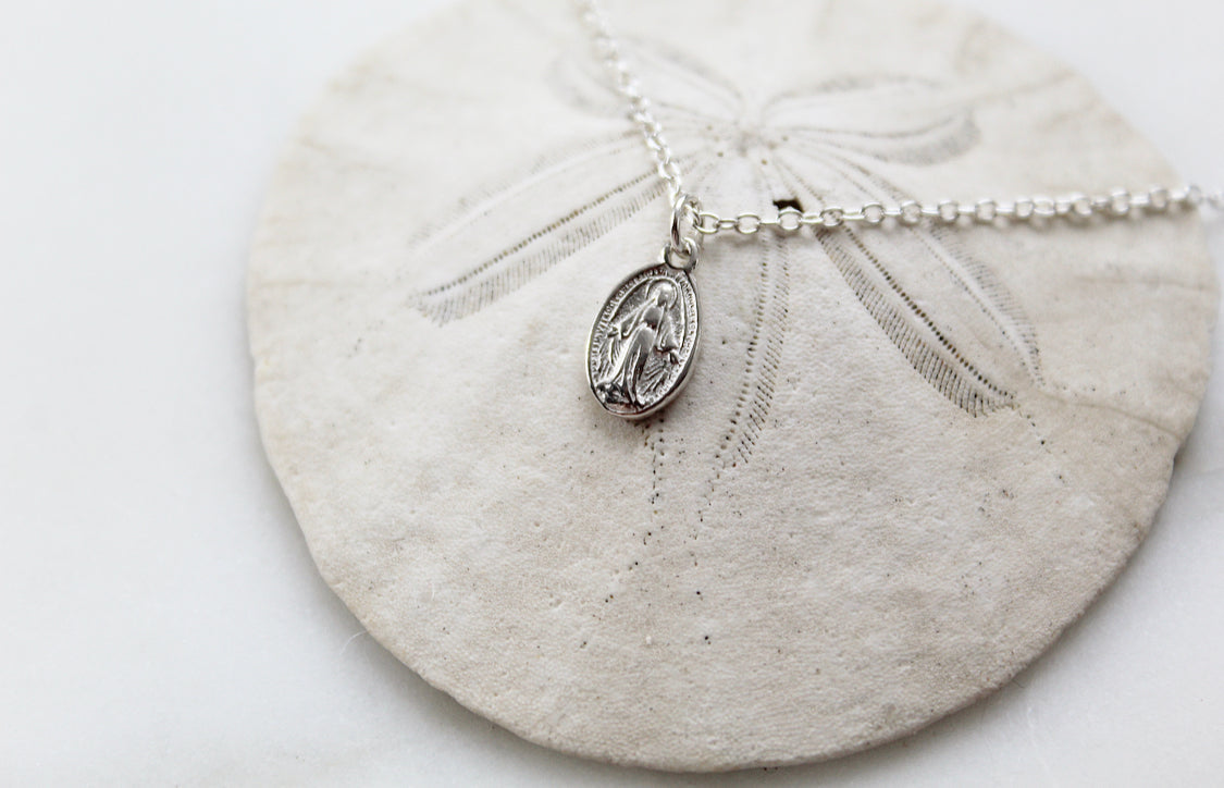 Miraculous medal pendant with oval shape on silver-tone chain, flat lay