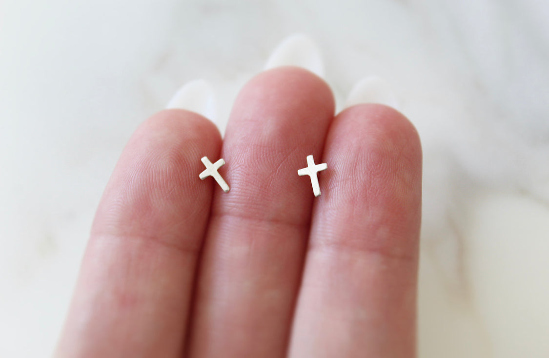 Sterling silver cross stud earrings on fingertips, three small cross charms visible.