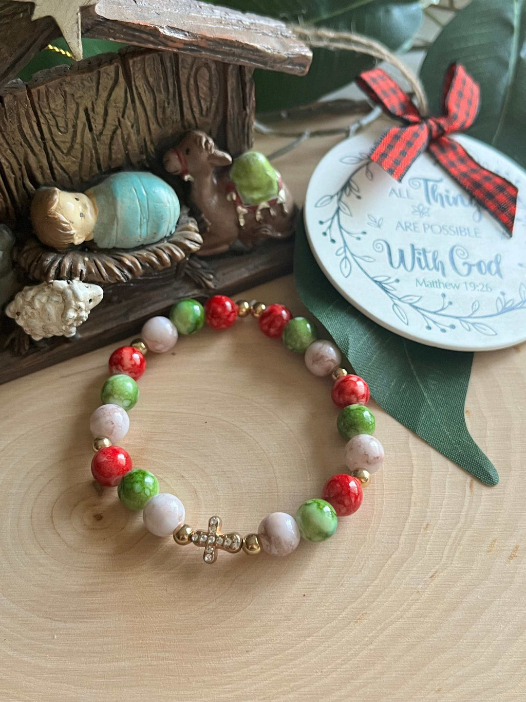 Beaded bracelet with red, green, and white beads with a silver cross charm center