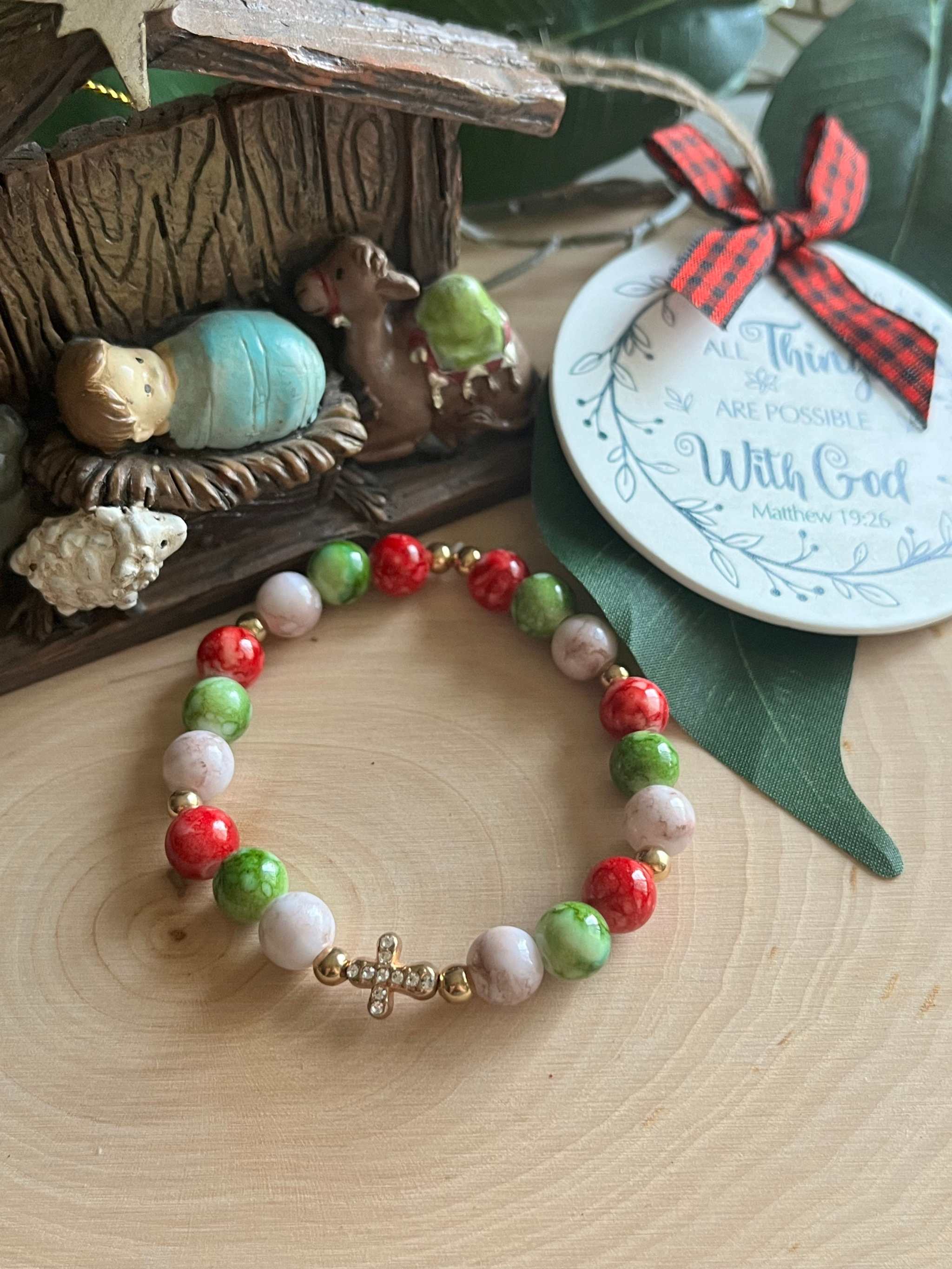 Beaded bracelet with red, green, and white beads with a silver cross charm center