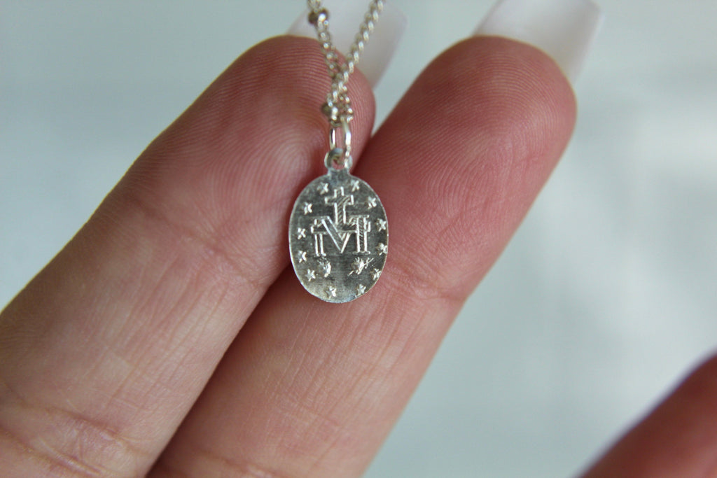 Silver oval medal necklace pendant with cross details and fine chain, held in palm