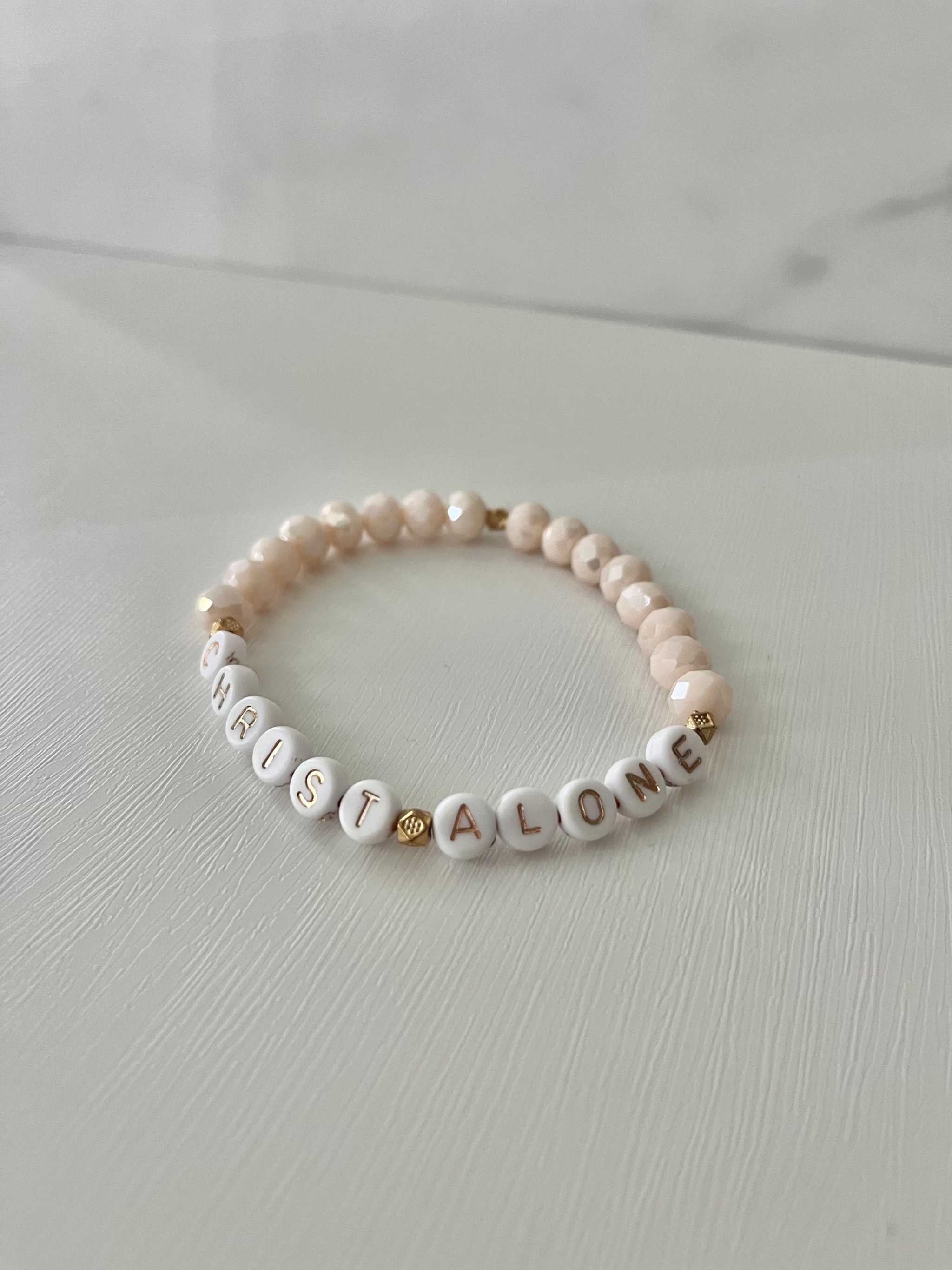 Peach-toned stretch bead bracelet with “Christ Alone” letter beads