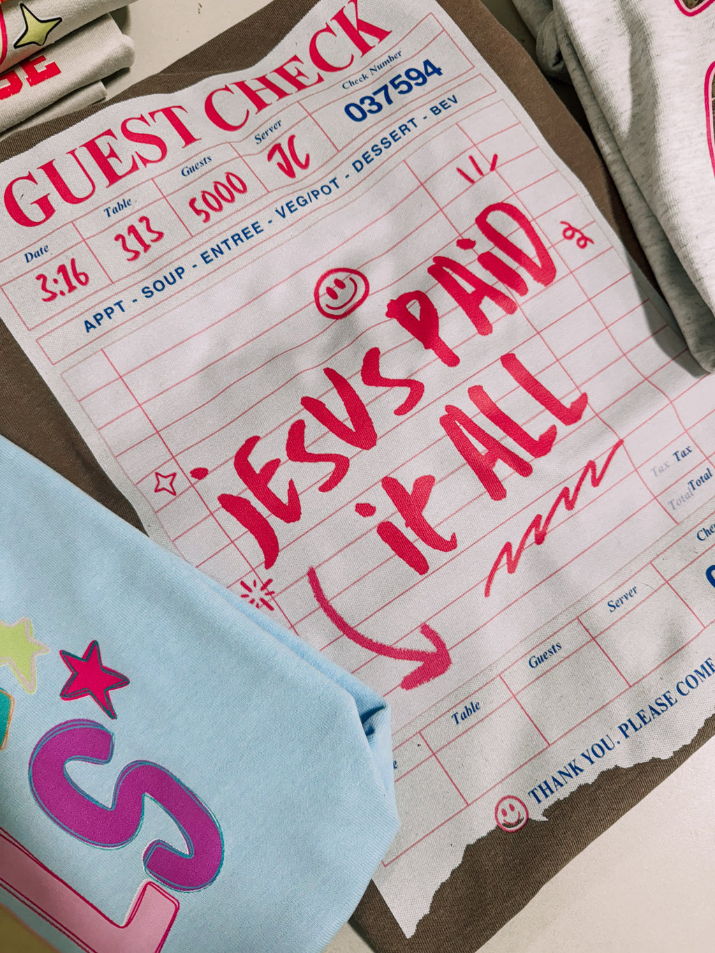 Light blue tee with 'Guest Check' graphic and red 'Jesus paid it all' lettering
