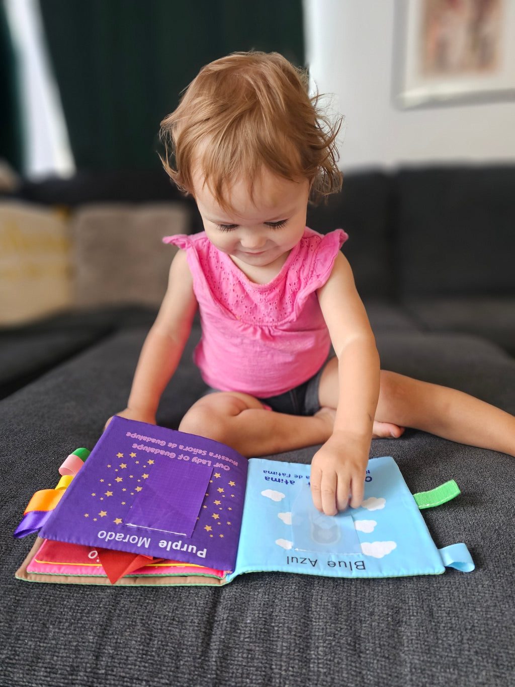 Toddler playing with an open purple fabric Mary book on a couch.