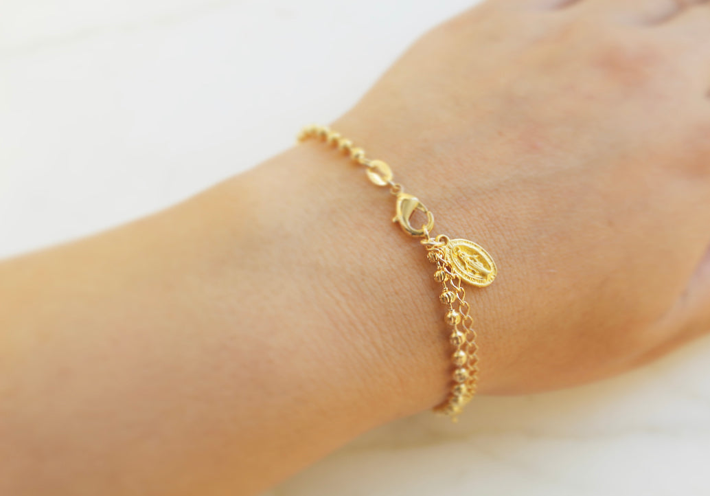 Gold-tone bracelet with ornate oval charm, worn on wrist