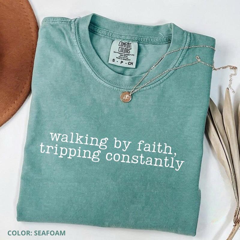 Women’s crewneck graphic tee, seafoam green with “walking by faith, tripping constantly”