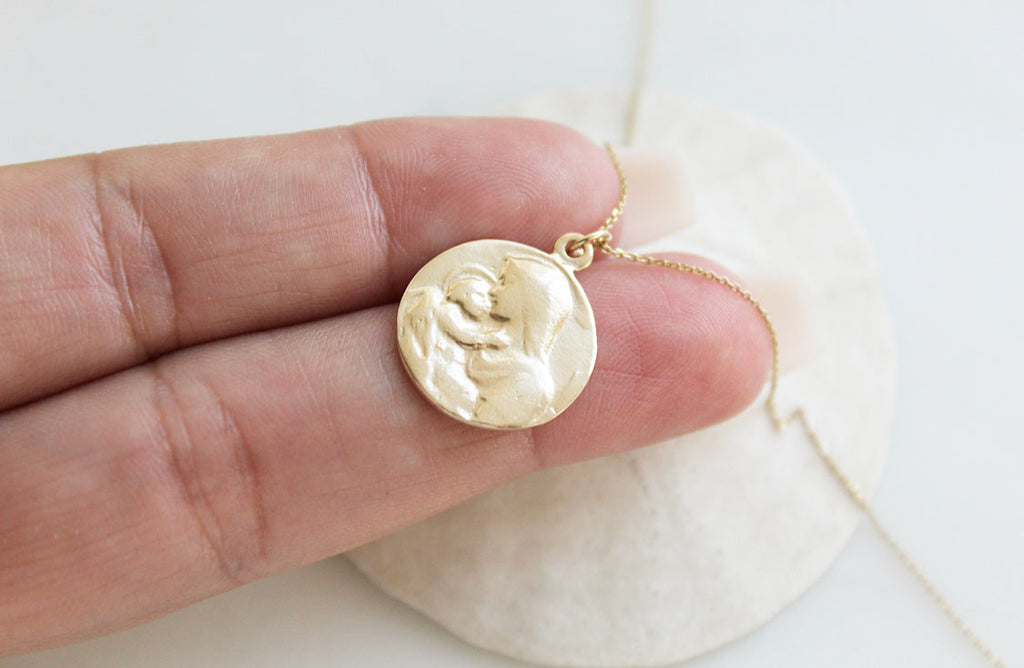 14k gold medallion pendant necklace with Jesus and Mary relief, close-up on hand