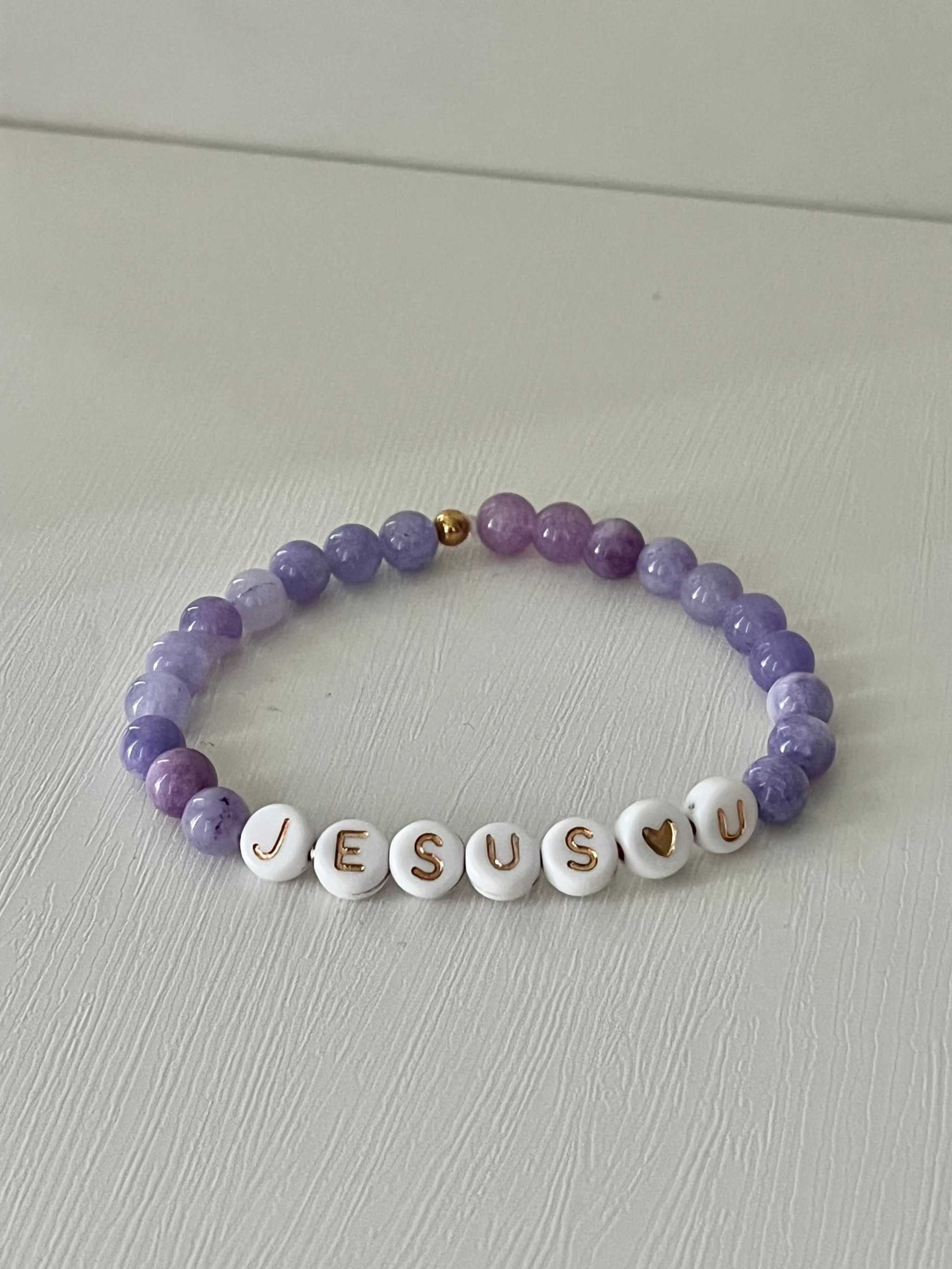 Purple bead bracelet with white letter beads spelling "JESUS U" and a heart charm