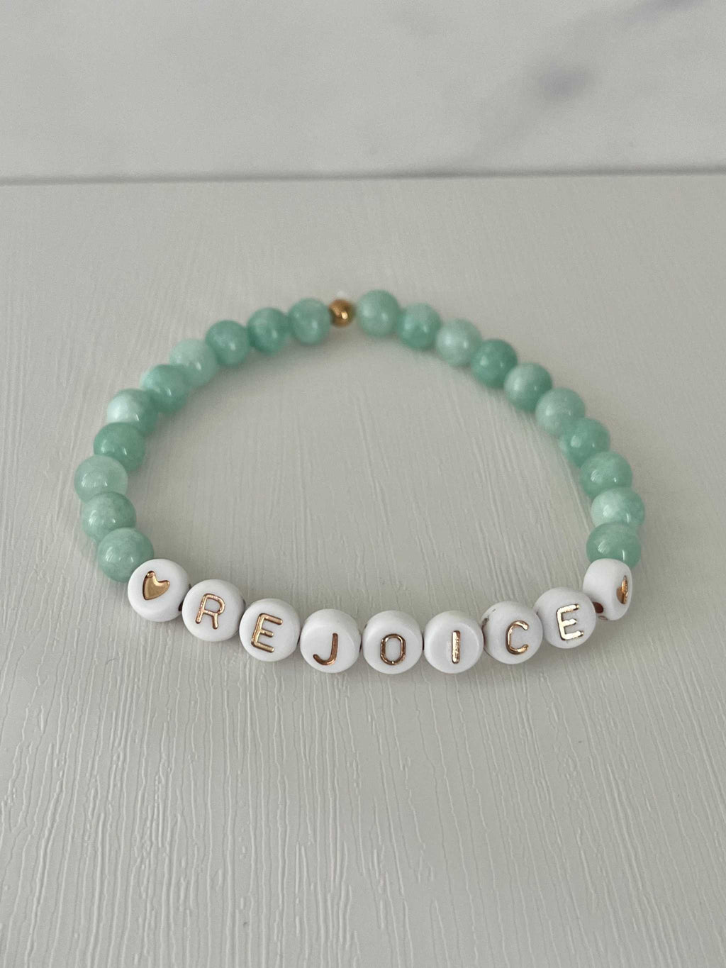 Green jade bracelet with white letter beads spelling REJOICE and gold accents