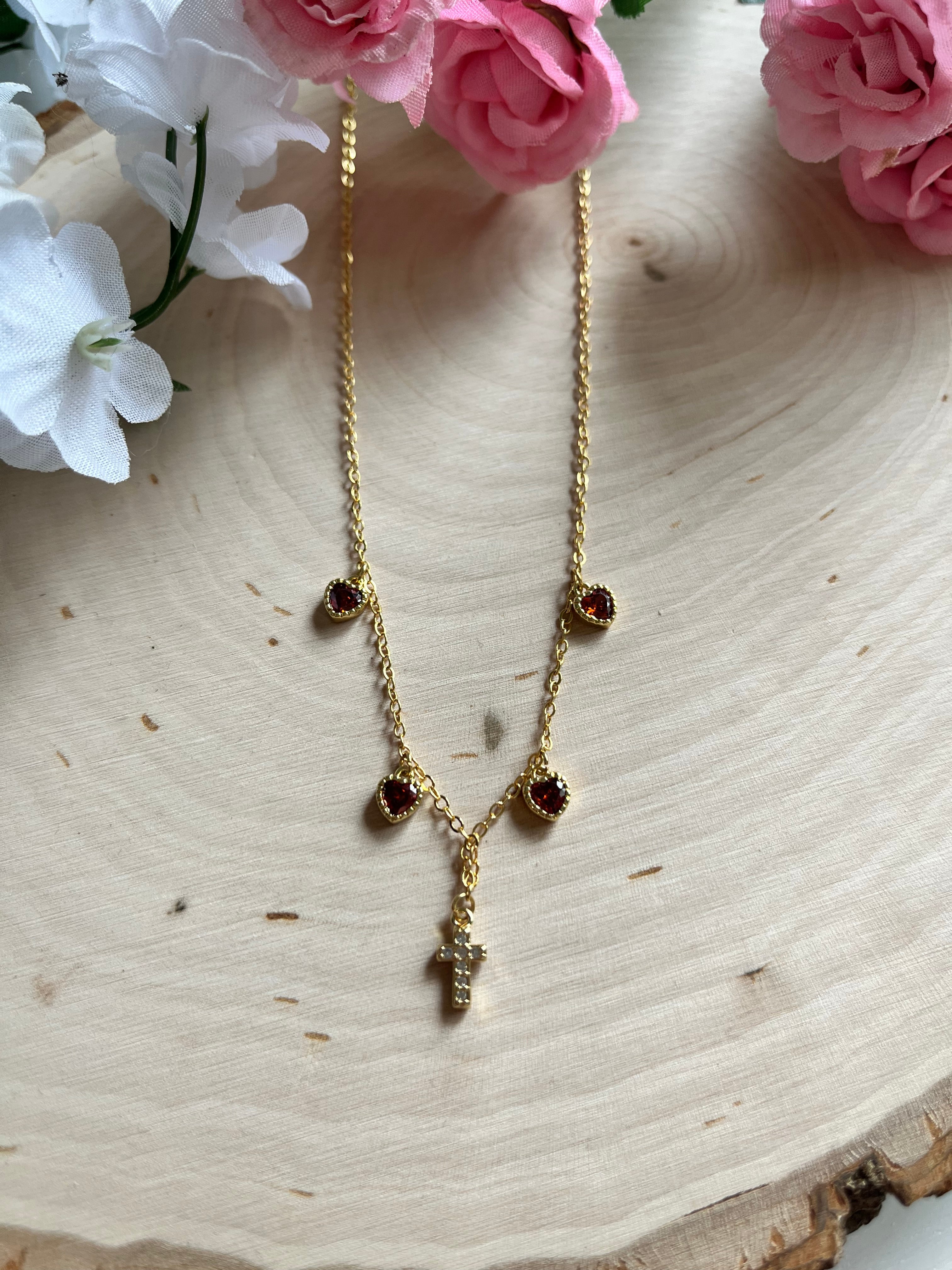 Gold charm necklace with red heart stones and small gold cross pendant, close-up