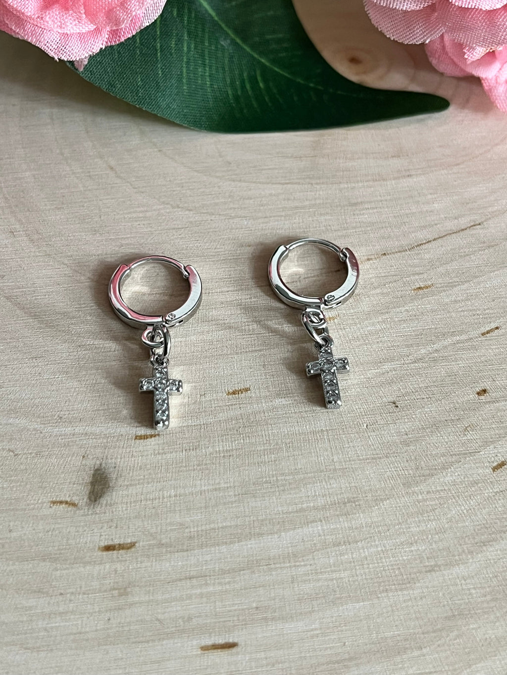 Silver huggie hoop earrings with cross charms, side view on light wood