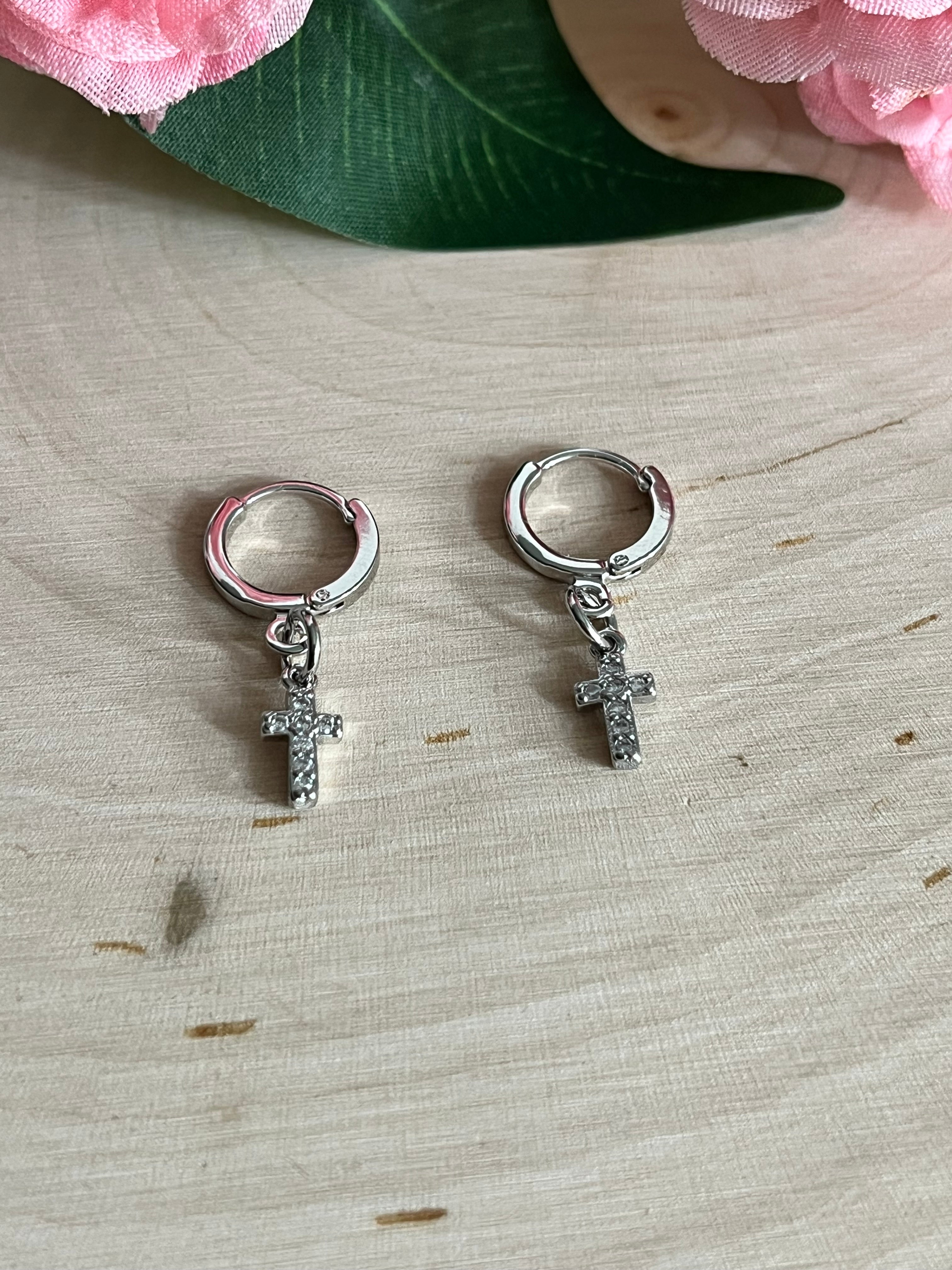 Silver huggie hoop earrings with cross charms, side view on light wood
