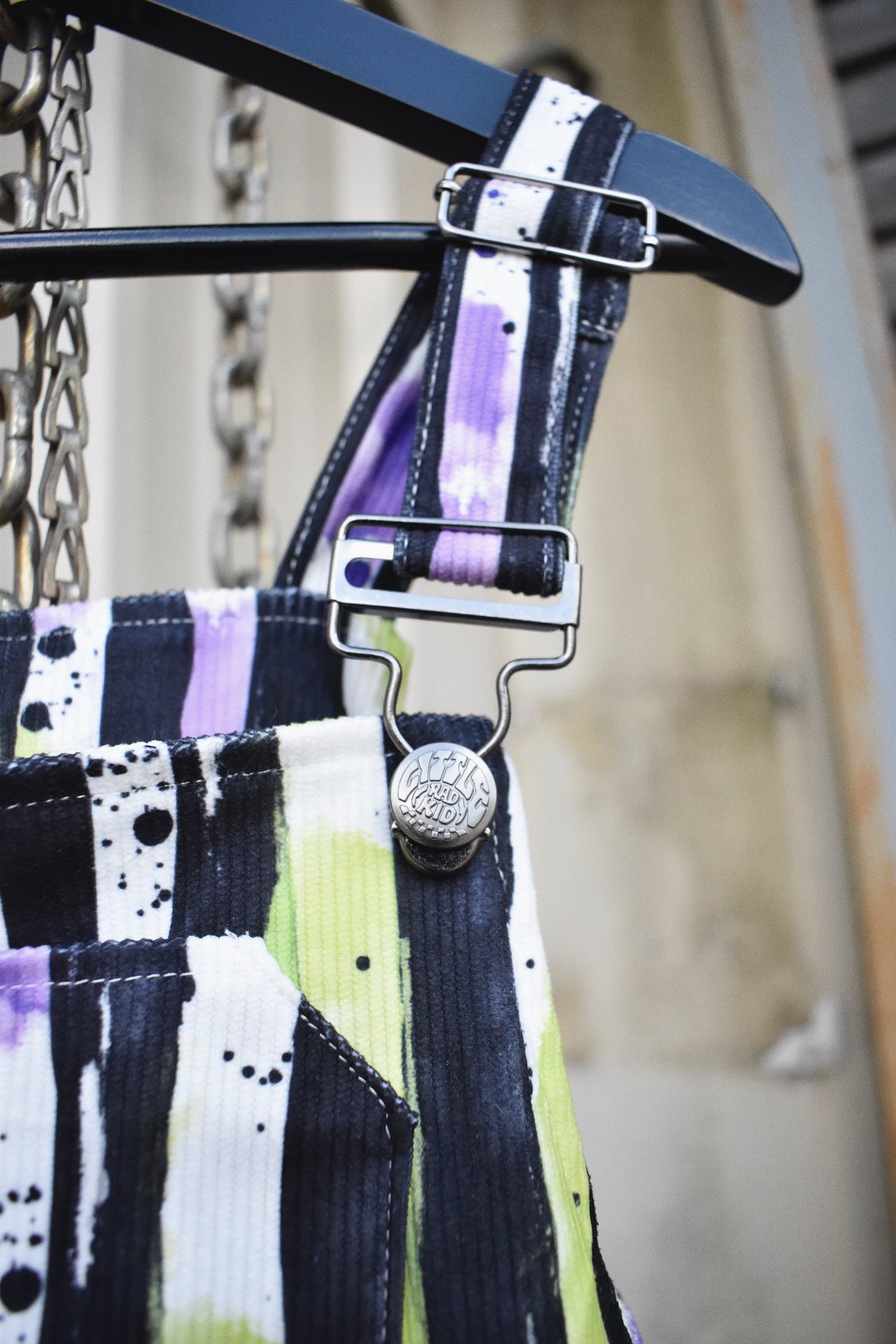Adjustable strap buckles on kids Halloween overalls with black, white, neon green stripes