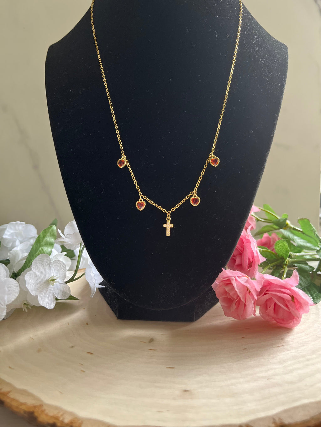 Gold charm necklace with red heart charms and gold cross pendant on a bust form