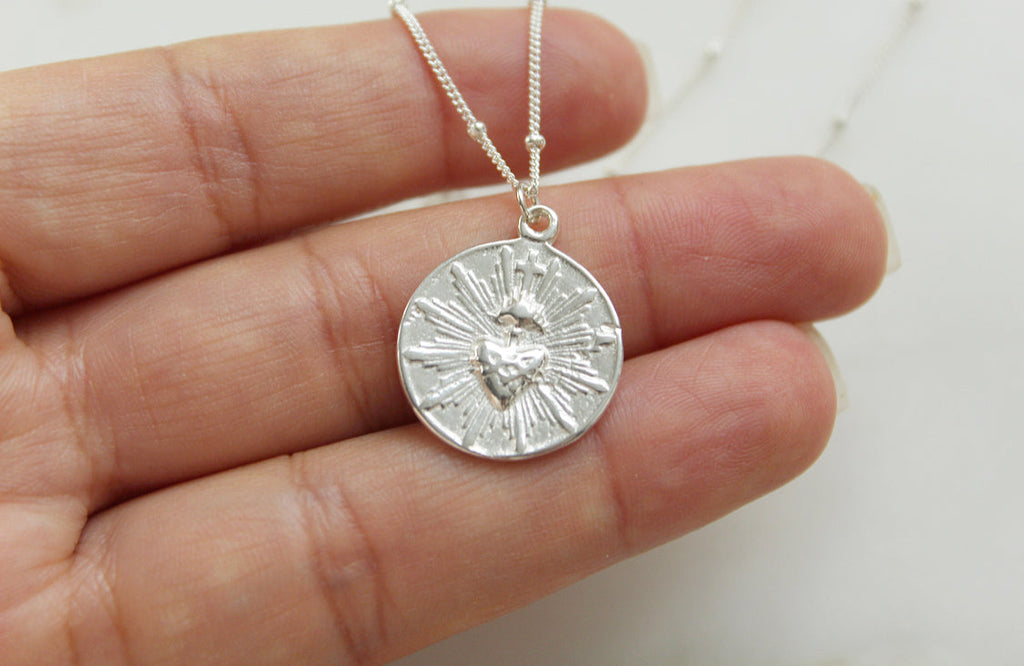 Silver round sacred heart coin pendant with radiating rays, on a fine chain.