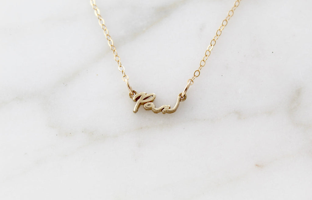 Gold Pax pendant necklace laid flat on light marble background