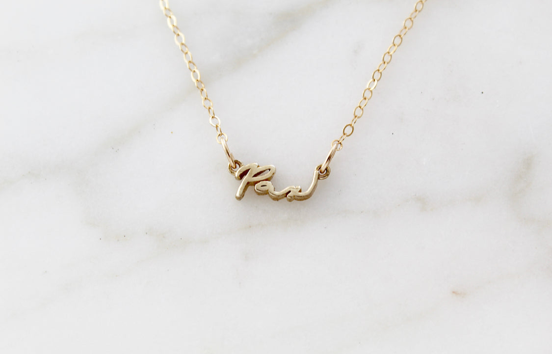 Gold Pax pendant necklace laid flat on light marble background