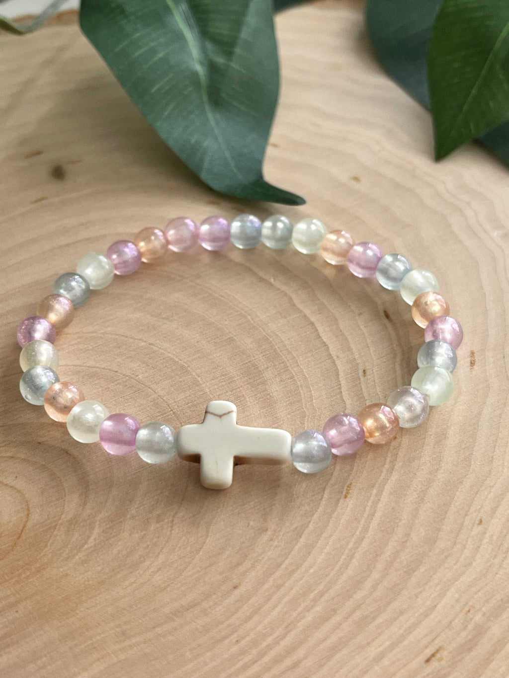Colorful beaded bracelet with a white cross charm in pastel pink, blue, and cream beads.