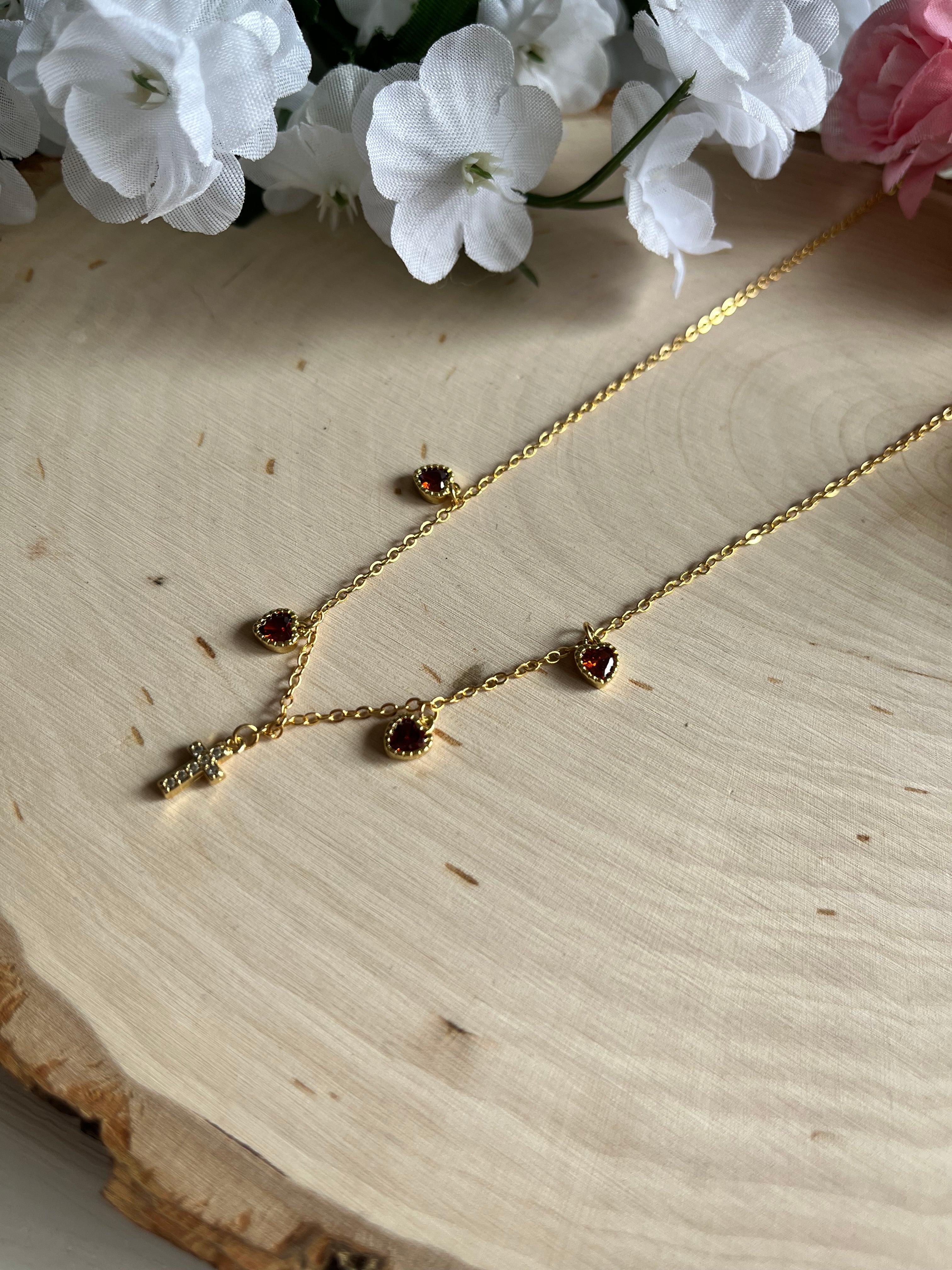 Gold charm necklace with red heart stones and cross pendant, chain laid flat