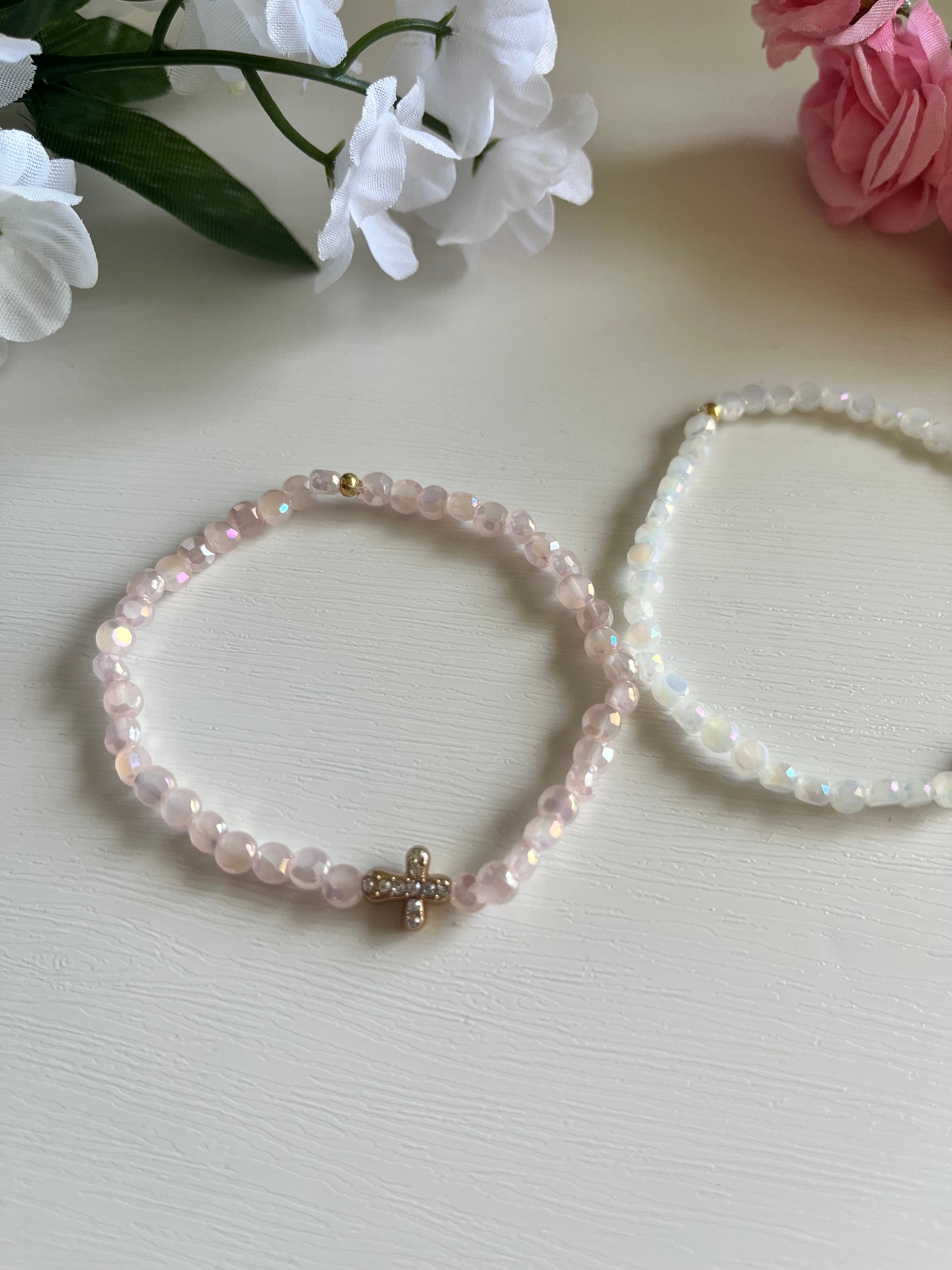 Two beaded bracelets: pink and white, each with a gold cross charm