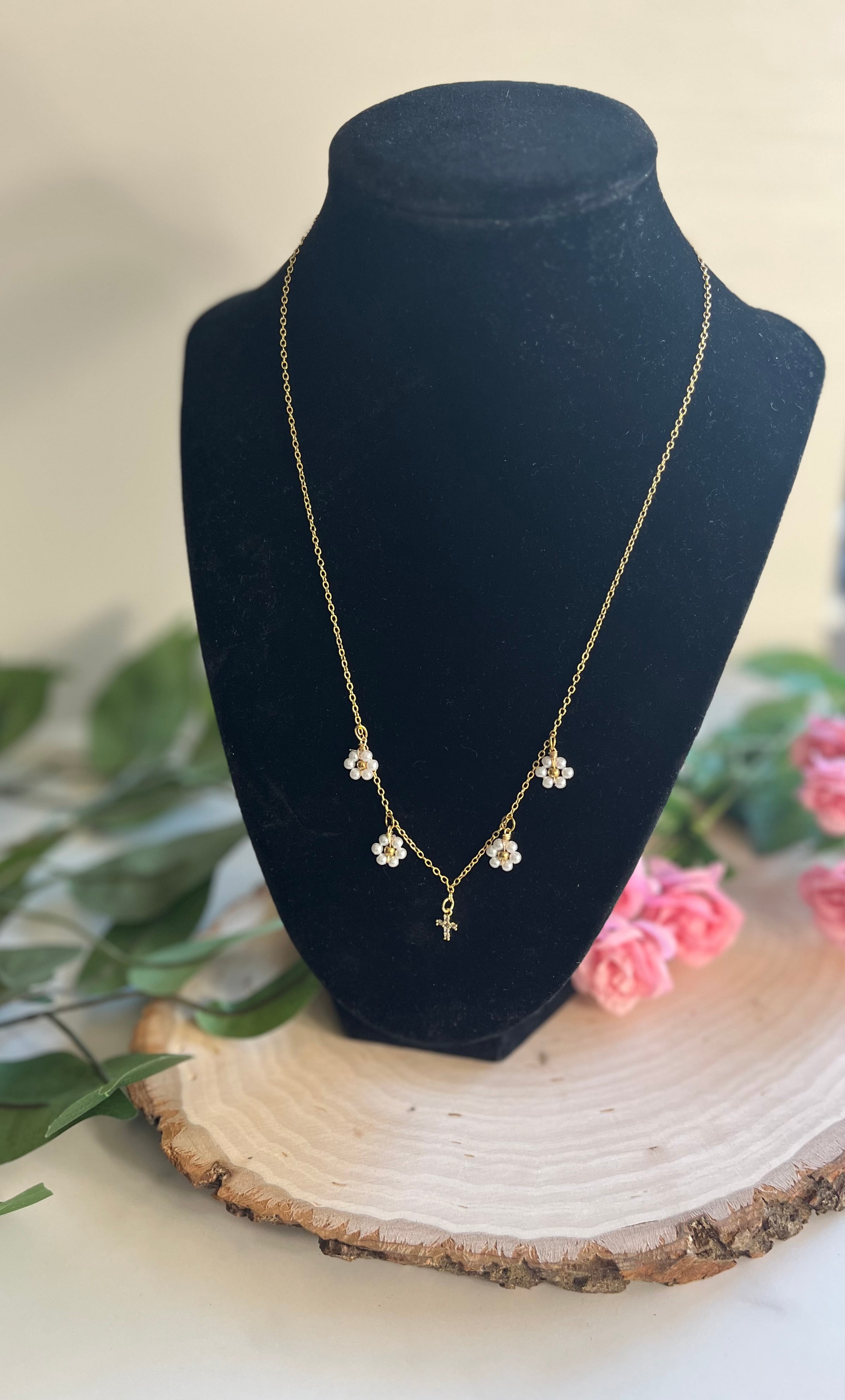 Gold cross pendant necklace with white daisy charms on a display bust