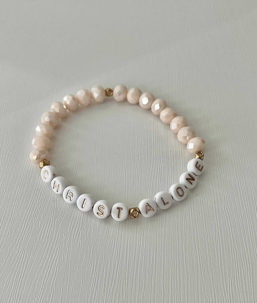 Peach-toned bead bracelet with “Christ Alone” letter beads and small heart charm