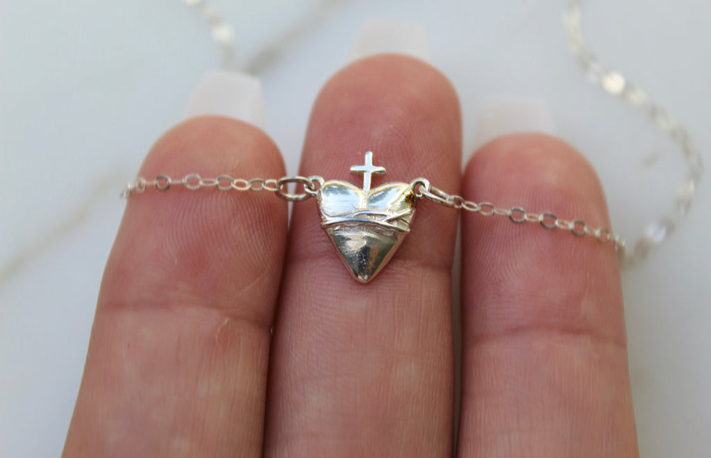 Sterling silver heart pendant with cross, chain clasp visible, held up by fingers