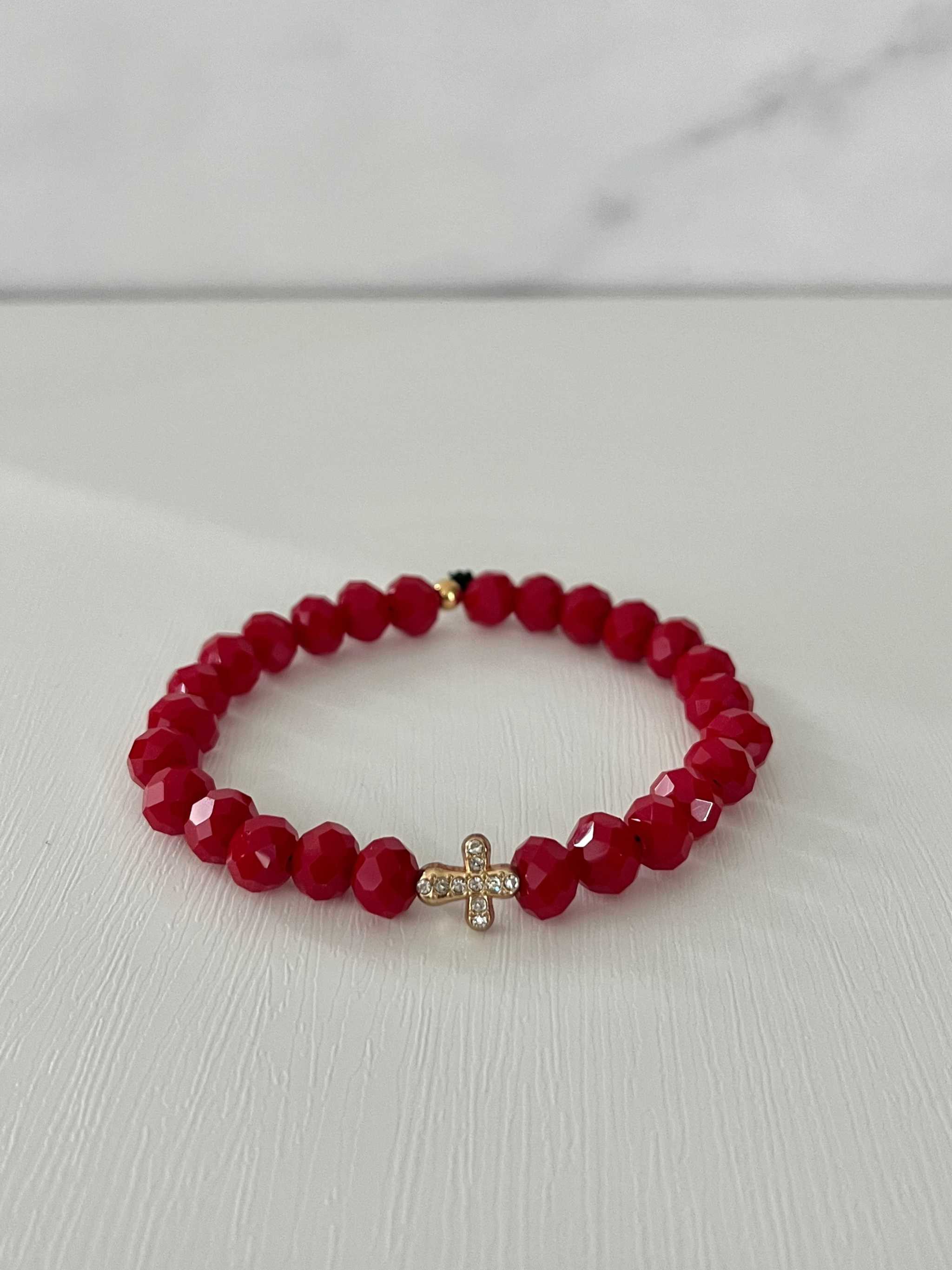 Red faceted bead cross bracelet with gold cross charm at center.
