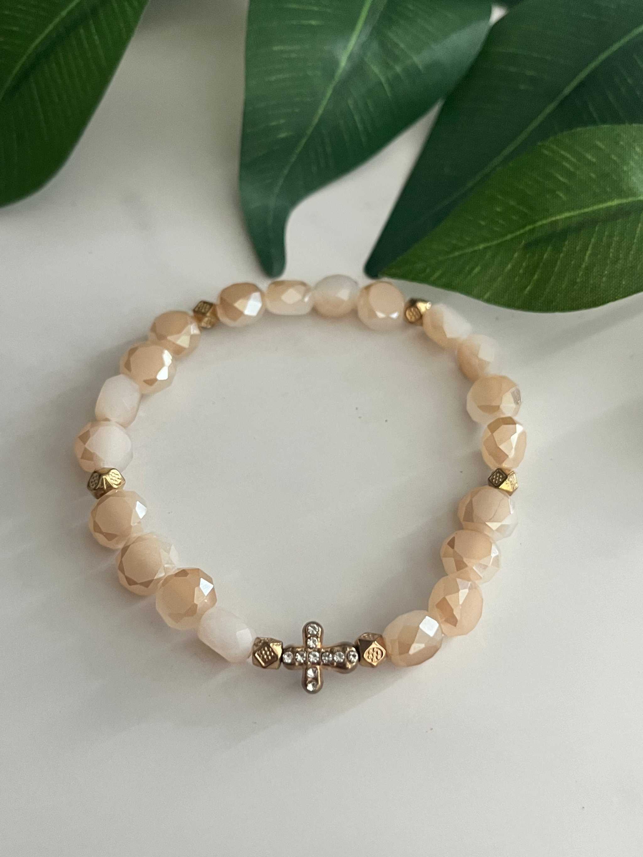 Cream and beige beaded bracelet with gold cross charm and faceted bead accents.
