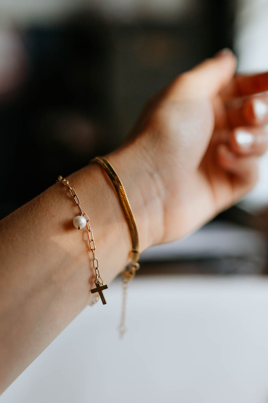 Gold-tone beaded bracelet on wrist with cross charm and small white pearl bead