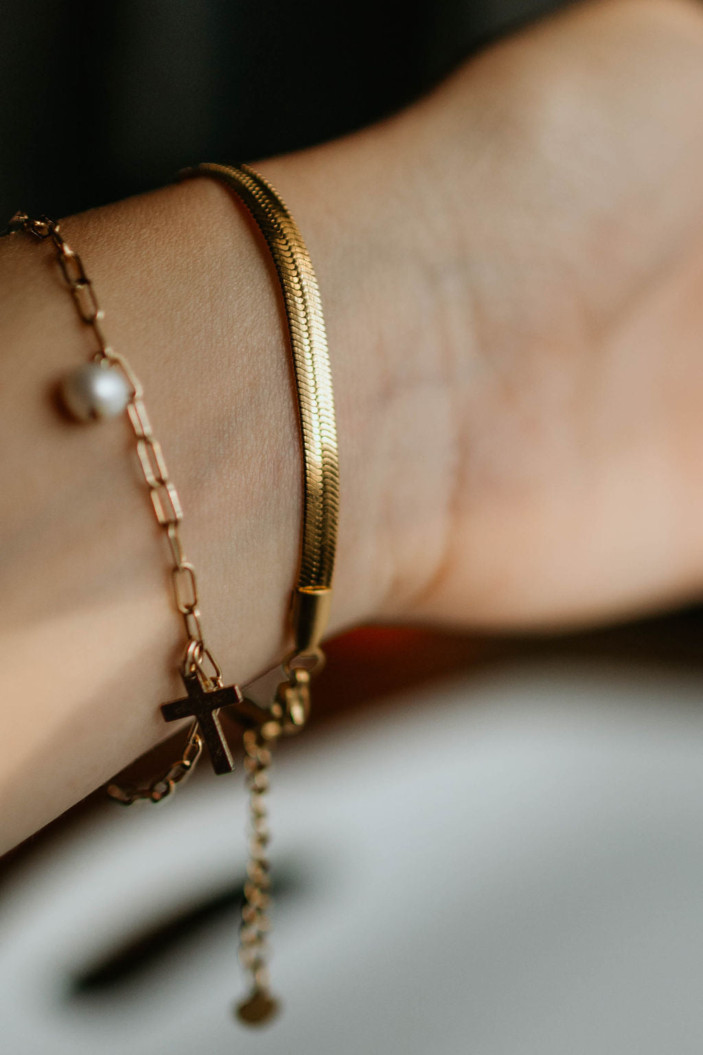 Gold-tone bracelet stack on wrist with cross charm and white pearl bead drops