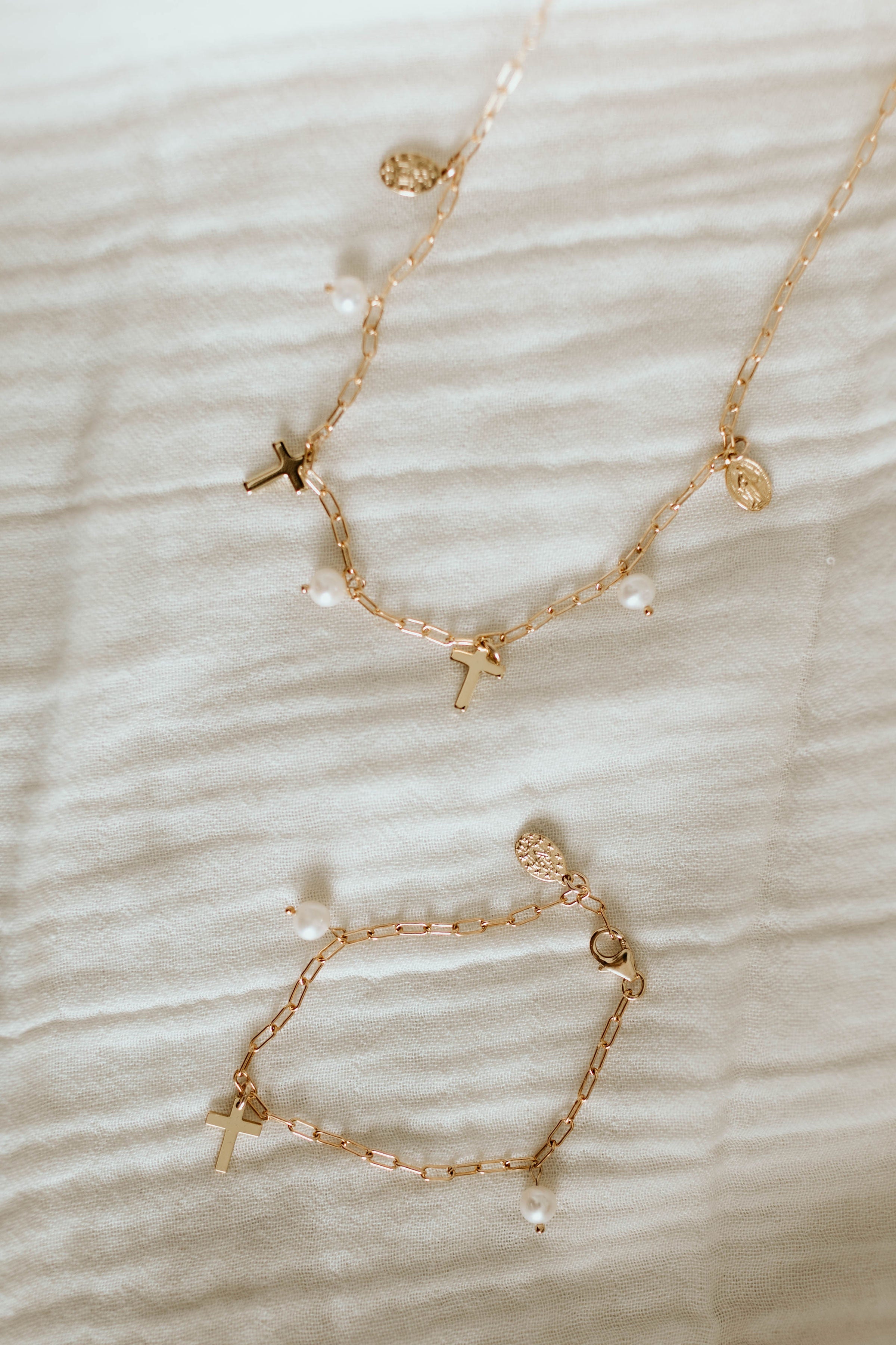 Gold-tone beaded bracelets with cross charms and white pearl drops laid on cloth