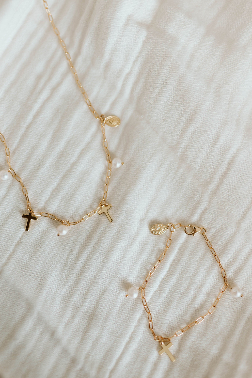 Gold-tone beaded bracelet and cross charms with white pearl accents on fabric