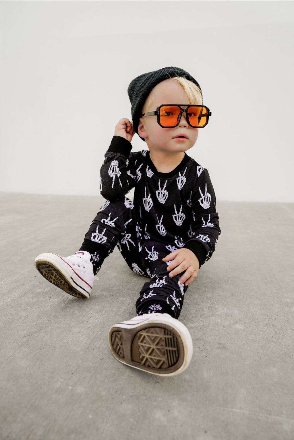 Kids black footed pajama set with white skeleton-hand pattern, long sleeves.
