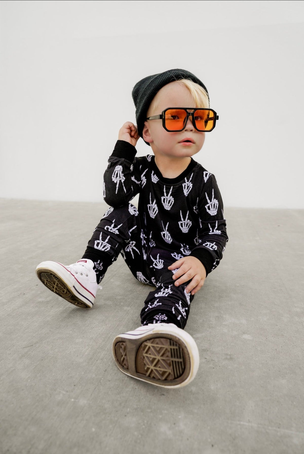Kids black footed pajama set with white skeleton-hand pattern, long sleeves.
