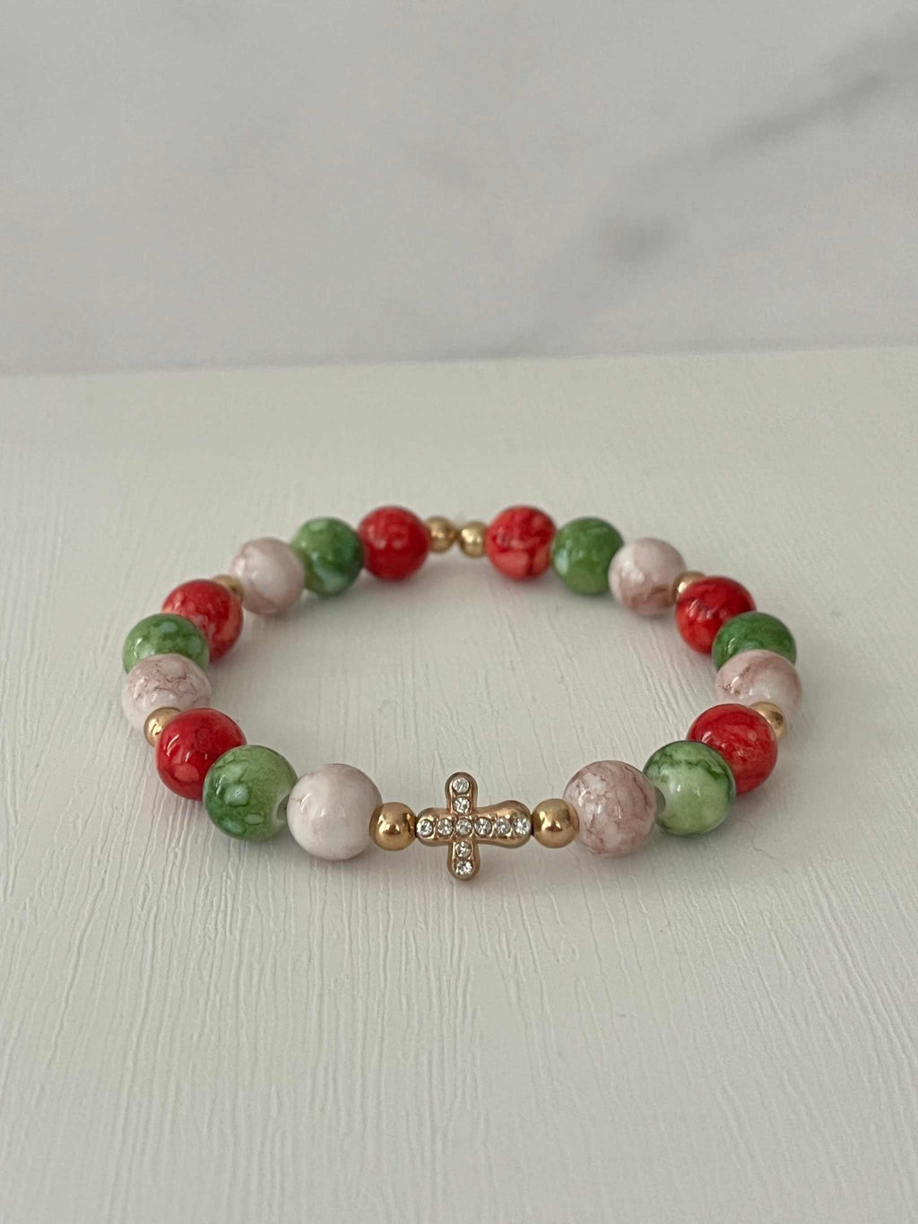 Bead bracelet with red, green, and white round beads and a gold jeweled cross center