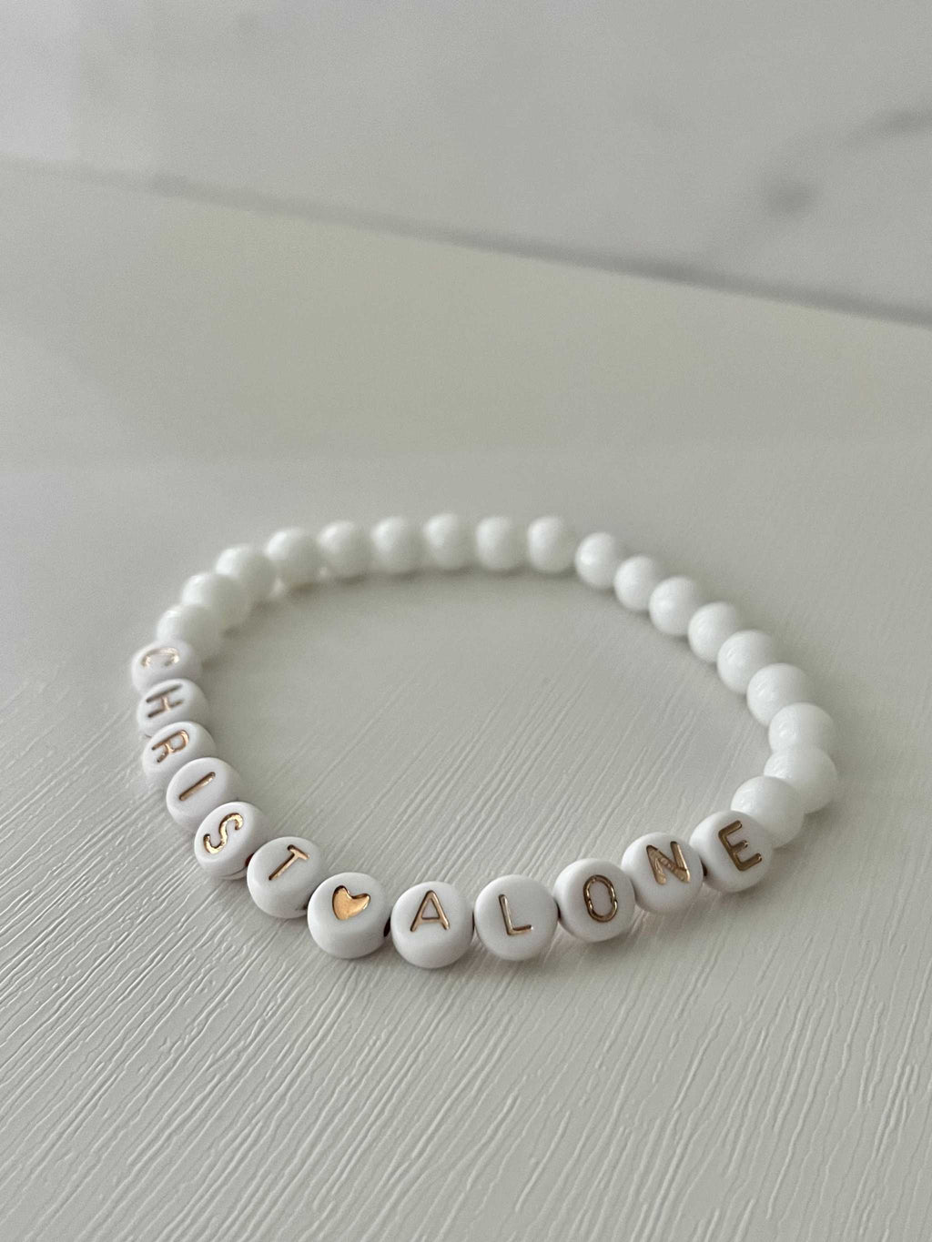 White bead bracelet with “Christ Alone” letter beads and heart accent
