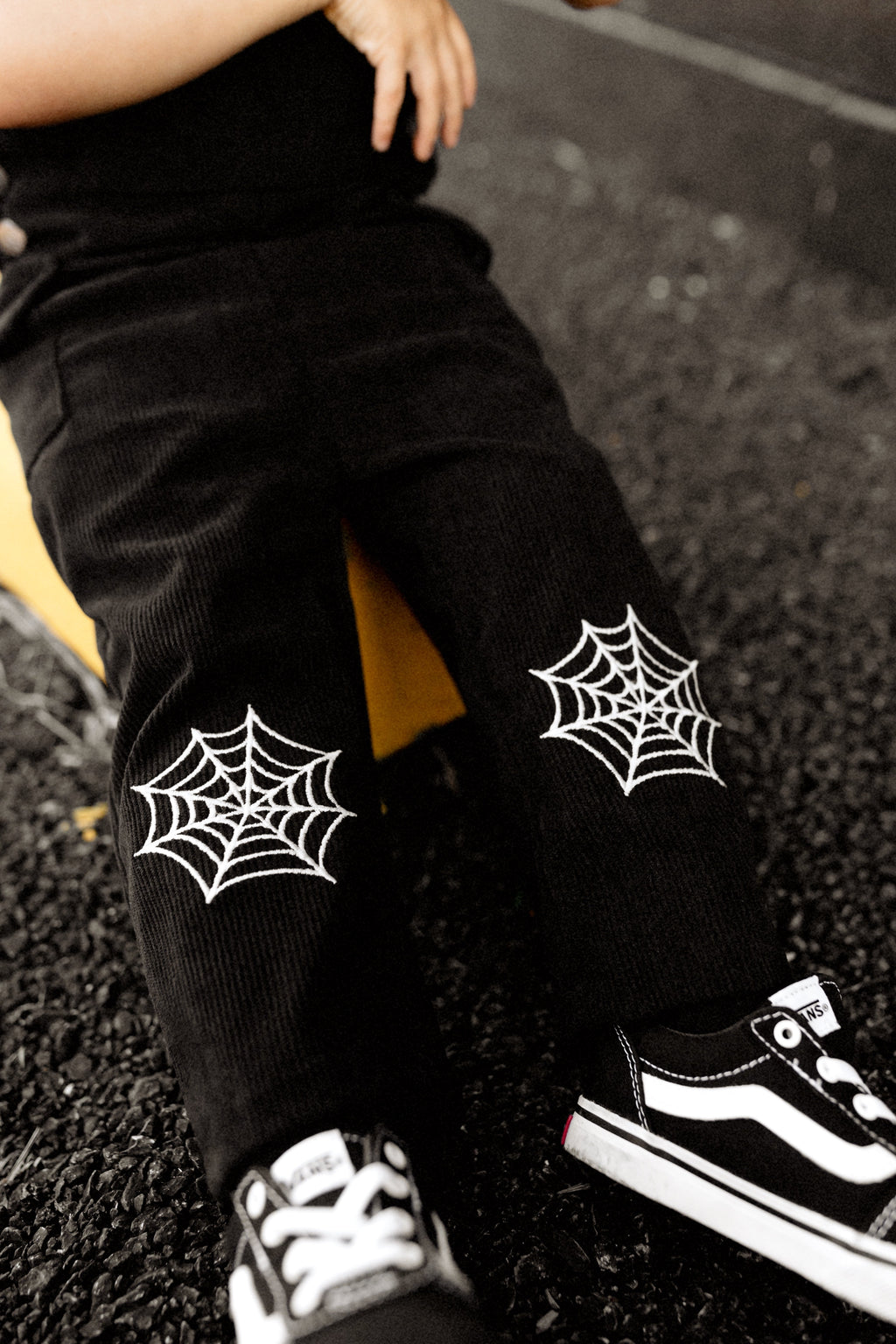 Close-up of black overalls legs with white spiderweb patches and cuffed hems.