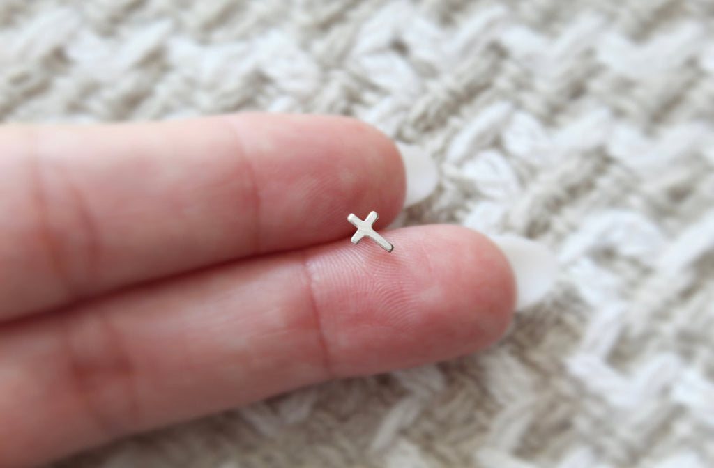 Sterling silver cross stud earring held between fingers, single cross charm visible.