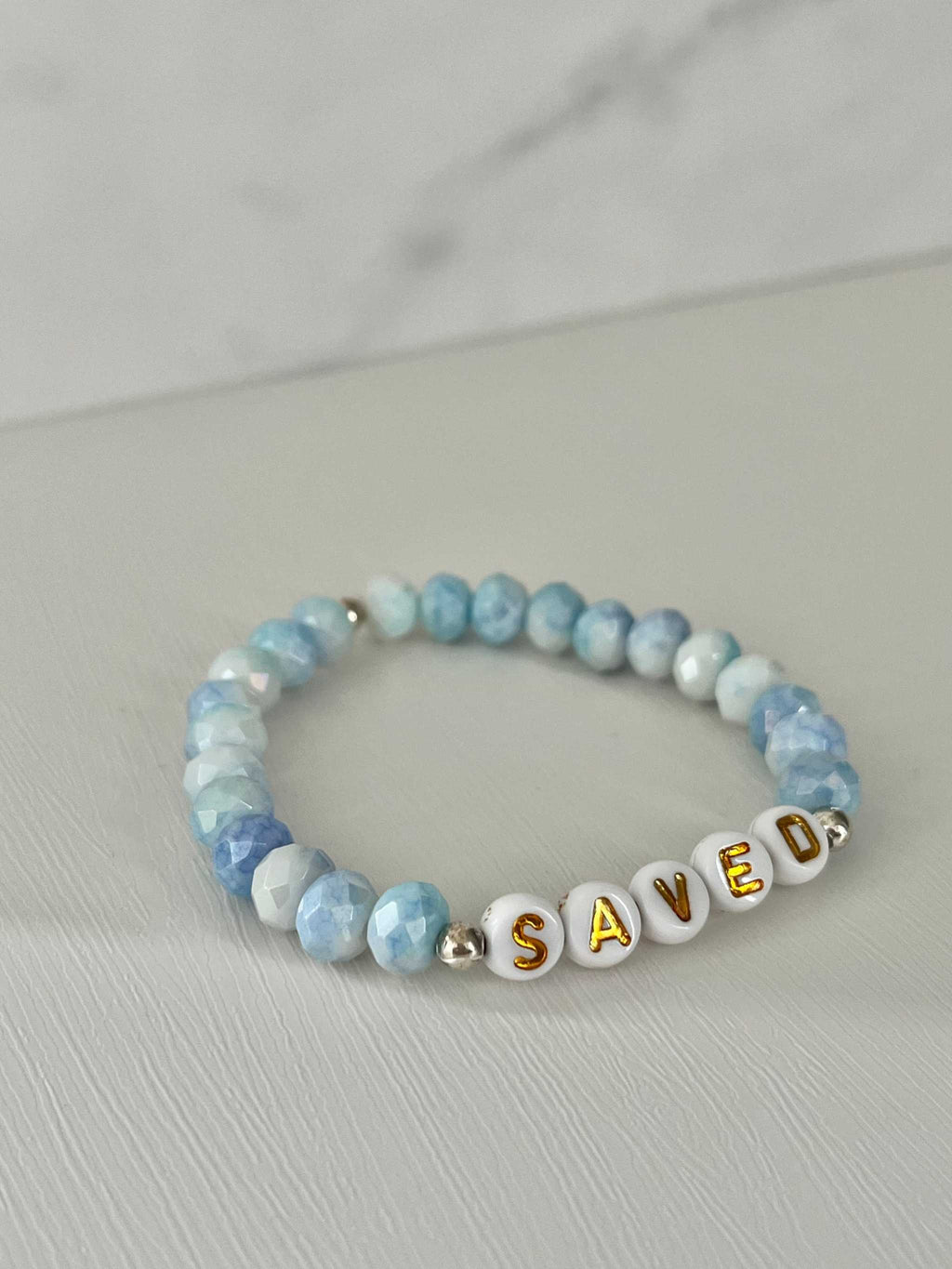 Light blue beaded bracelet with 'SAVED' letter beads and gold-tone spacers