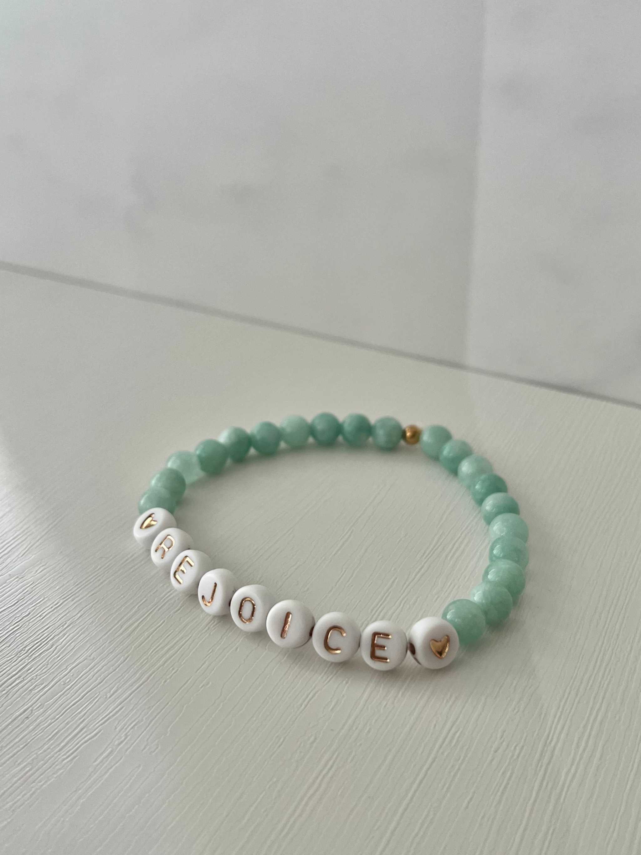 Green jade bead bracelet with white letter beads spelling REJOICE, small gold charms