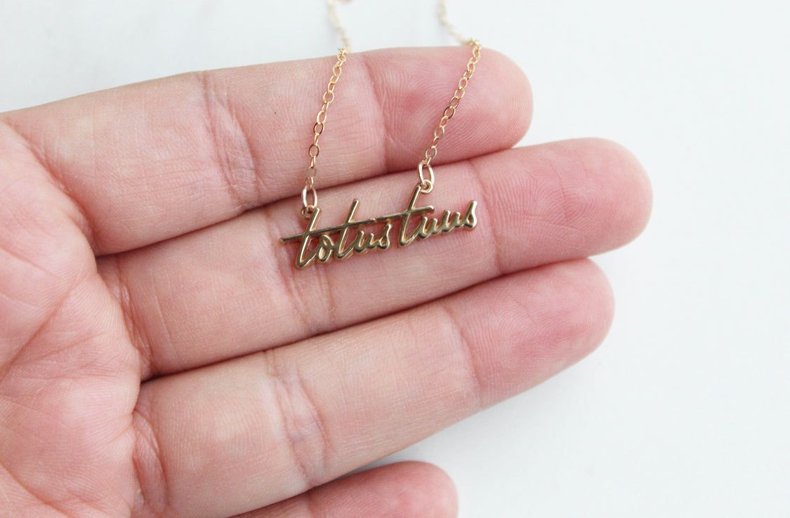 Gold-tone script pendant necklace with chain links in hand