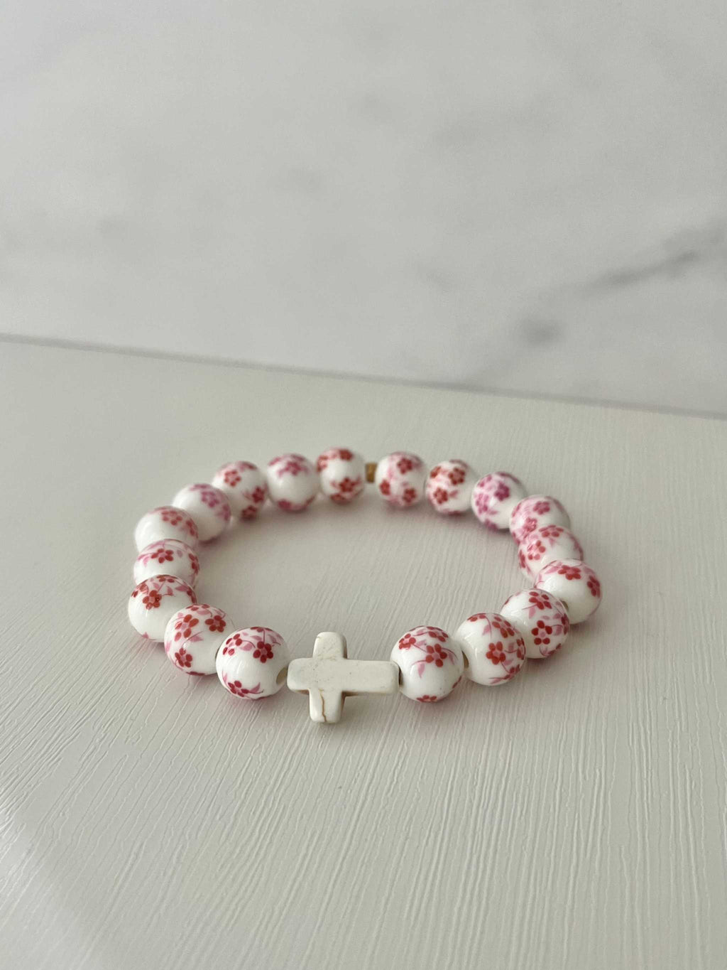 White bead bracelet with pink floral dots and a small white cross charm.