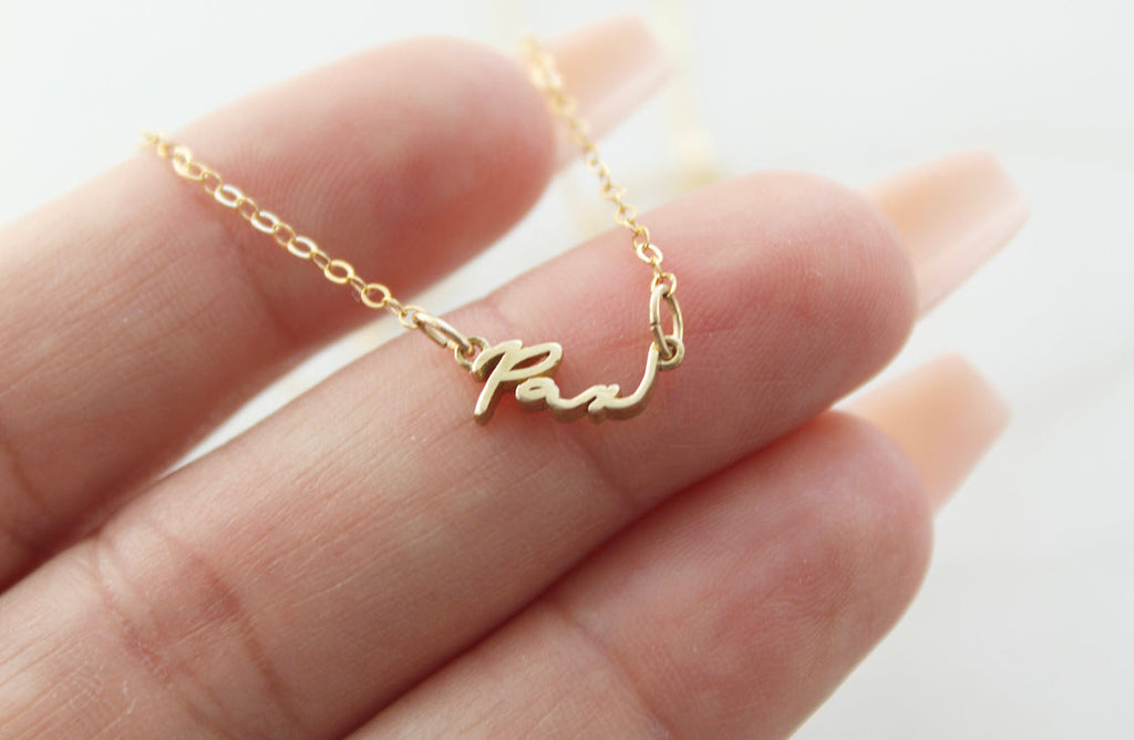 Gold Pax pendant necklace close-up on hand, polished pendant on link chain