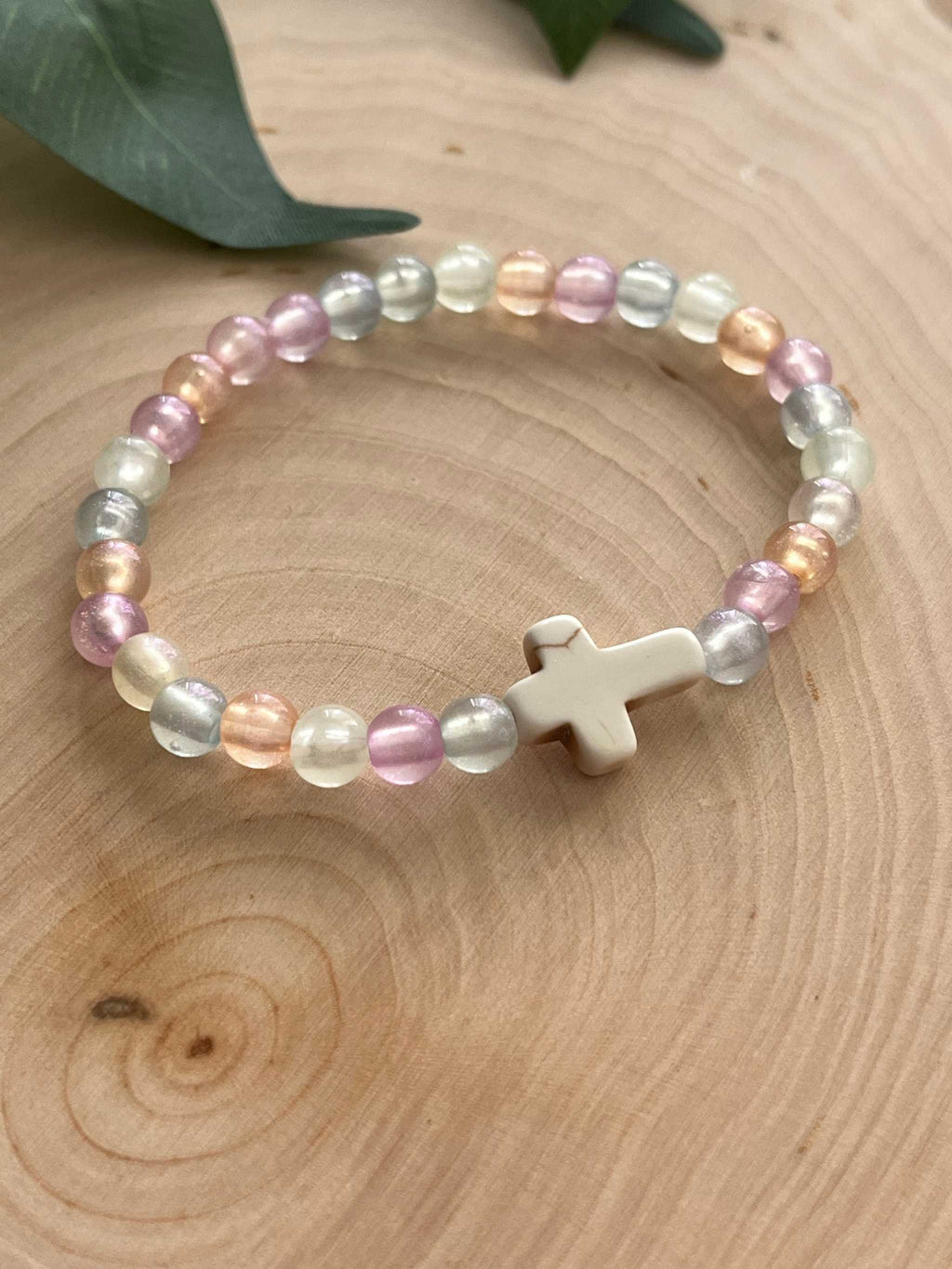 Pastel bead bracelet with white cross charm and mixed purple, blue, and cream beads.