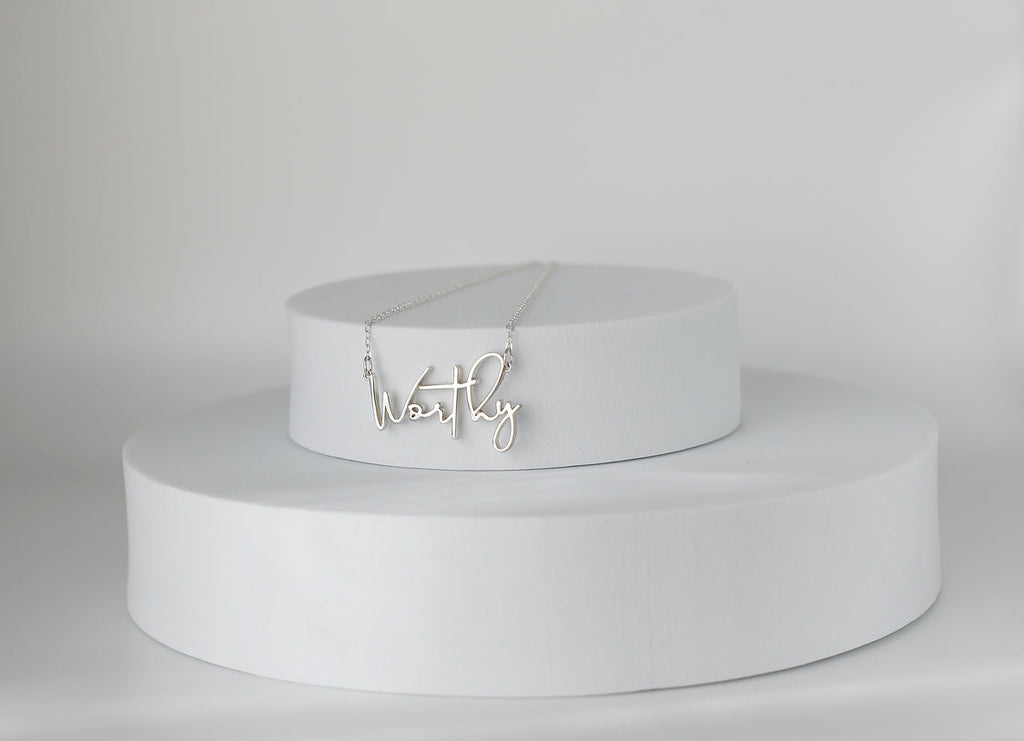Sterling silver Worthy pendant necklace displayed on two-tier pedestal