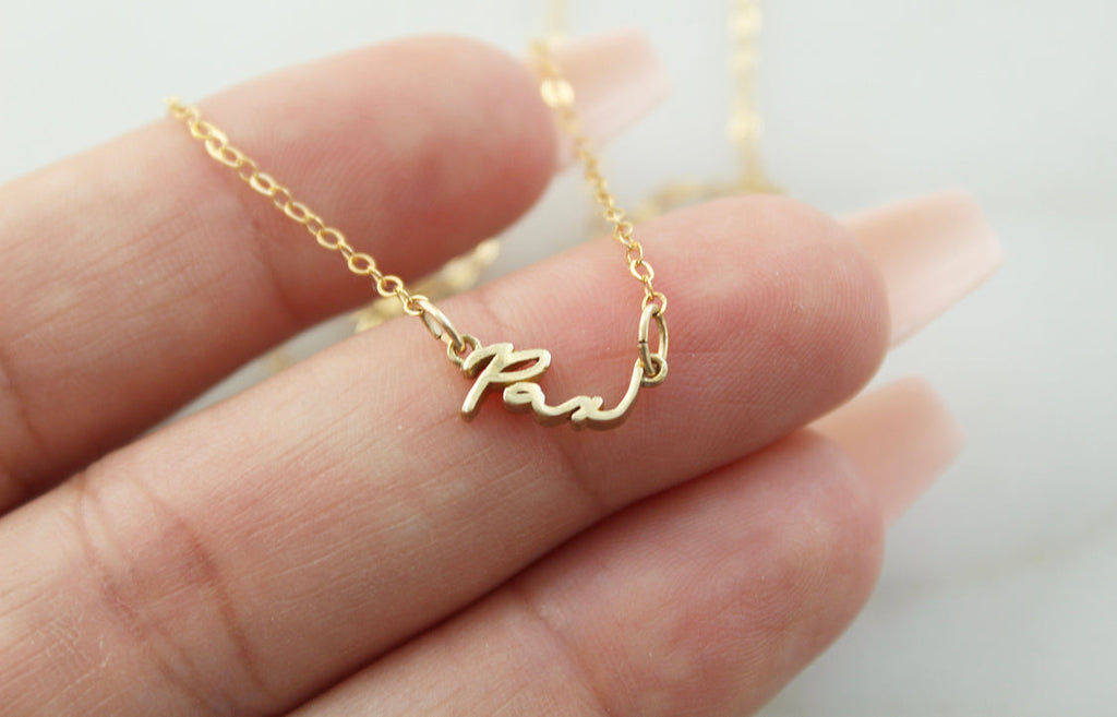 Gold Pax pendant necklace with link chain, shown on open palm close-up