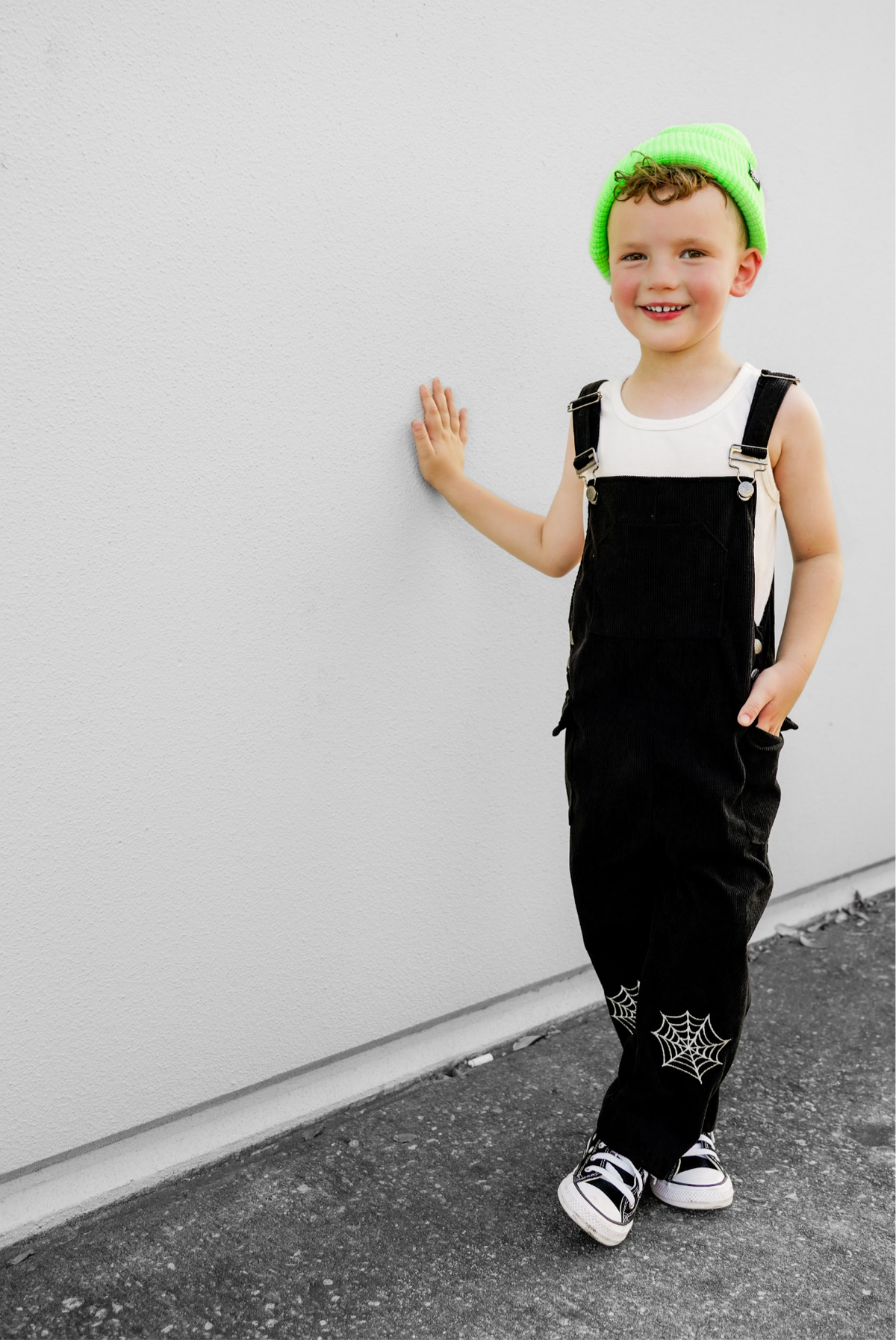 Black kids’ overalls with front bib straps and white spiderweb ankle patches.