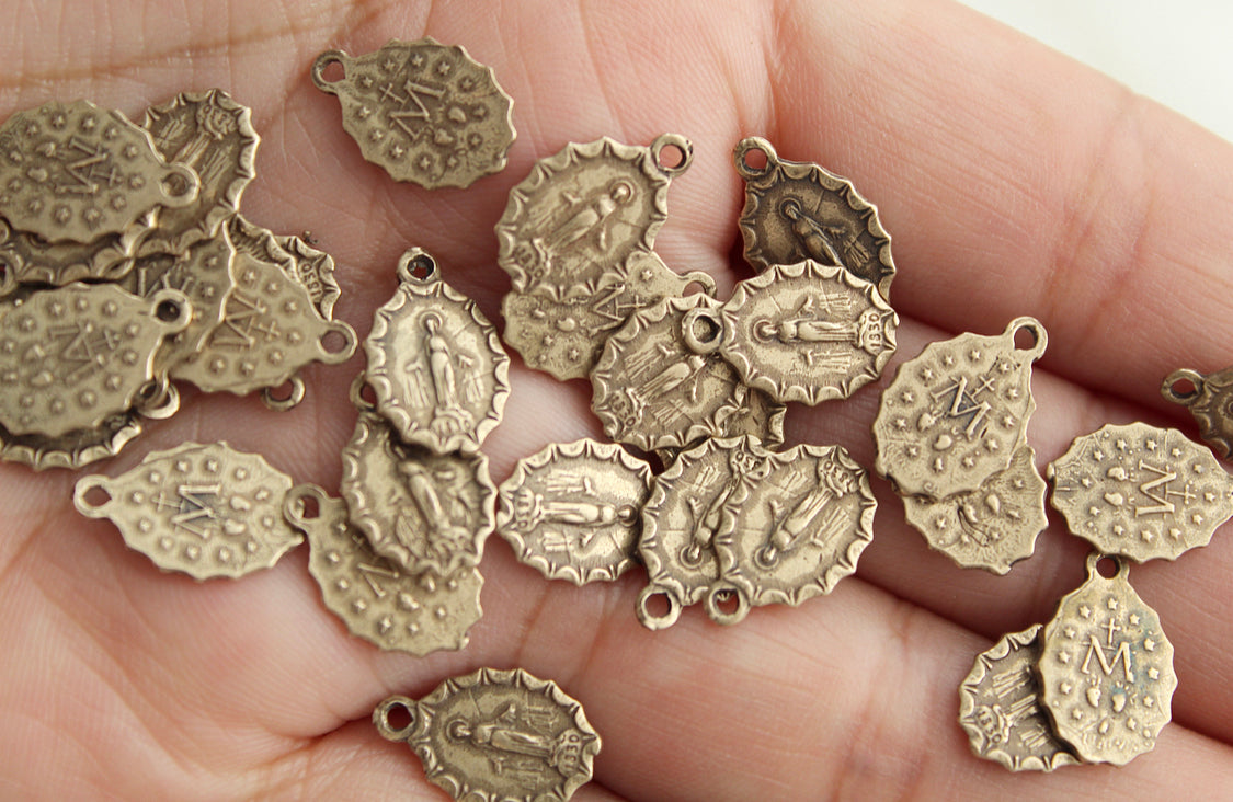 Assorted bronze medal charms with loops, close view held in hand.